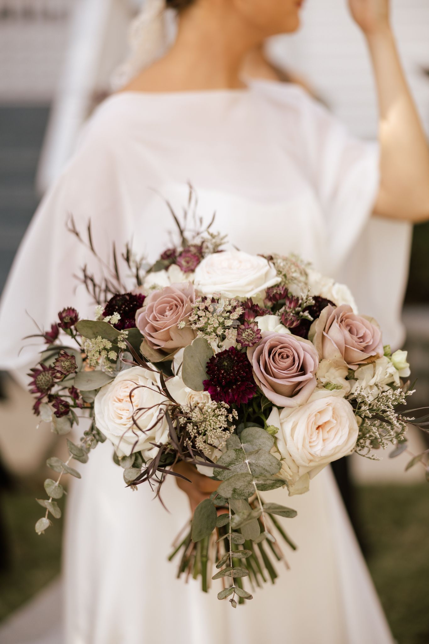 Romantic bridal bouquet featuring blush roses, burgundy flowers, and eucalyptus greenery.
