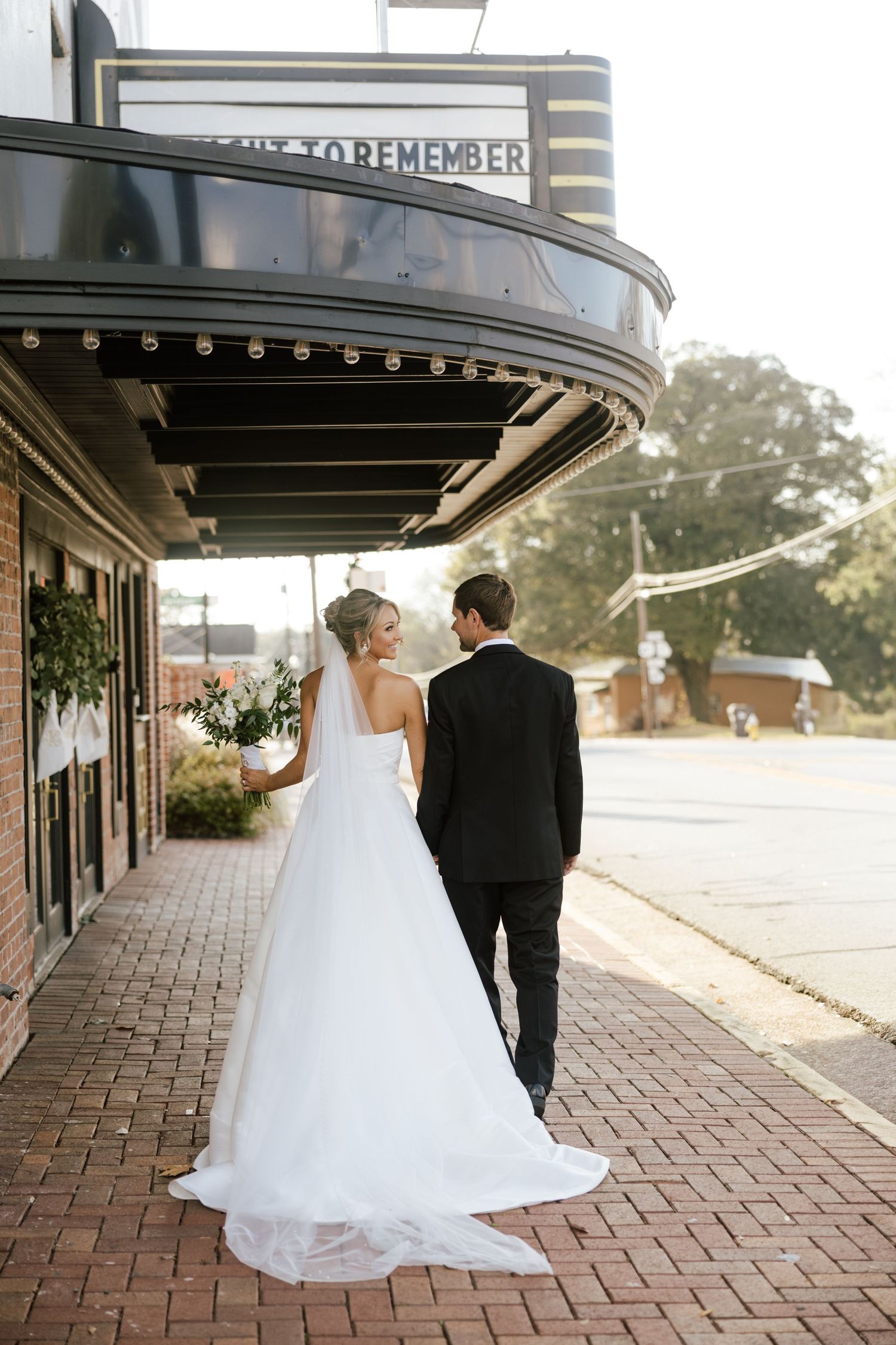 Bride and groom walking hand in hand outside a vintage theater marquee on their wedding day.
