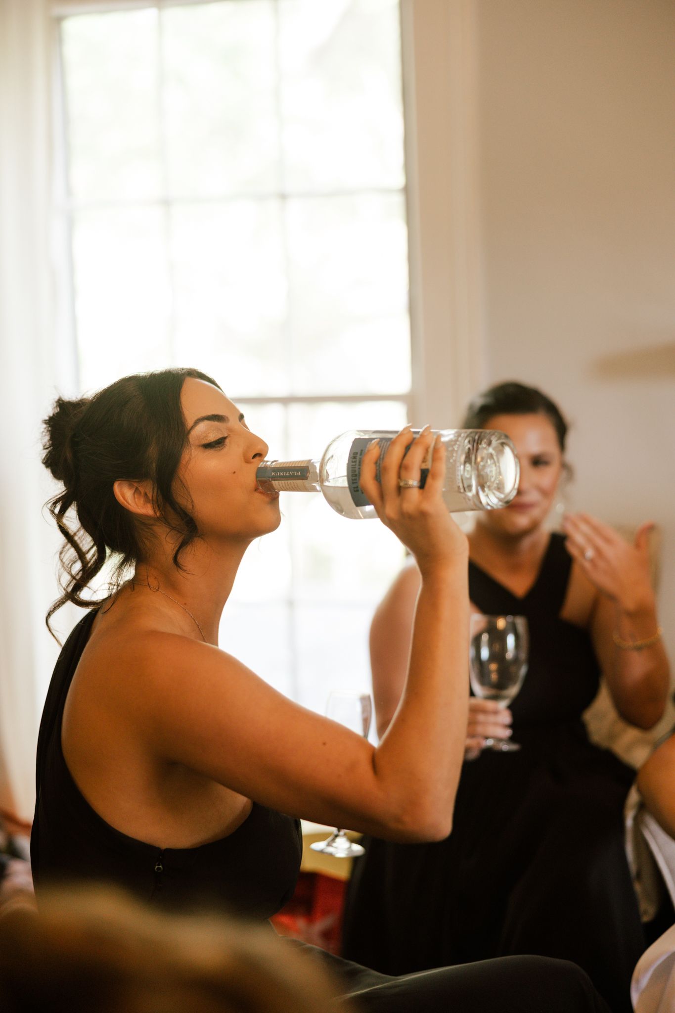 Wedding party members in black dresses drink from bottles during celebration.