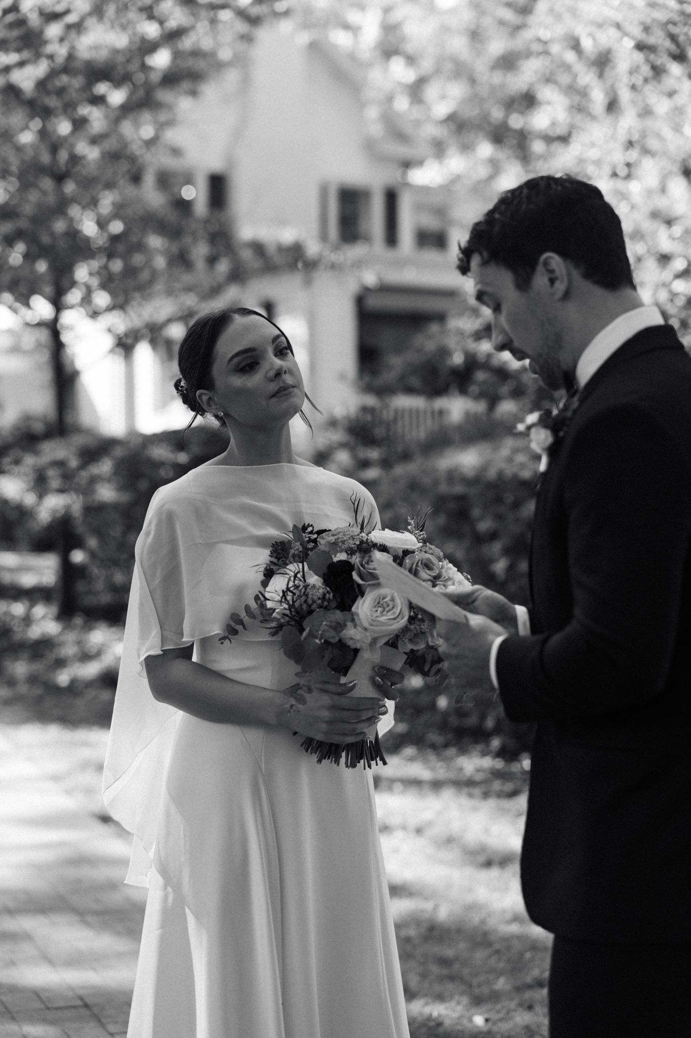 Black and white wedding portrait with couple holding bouquet outdoors.