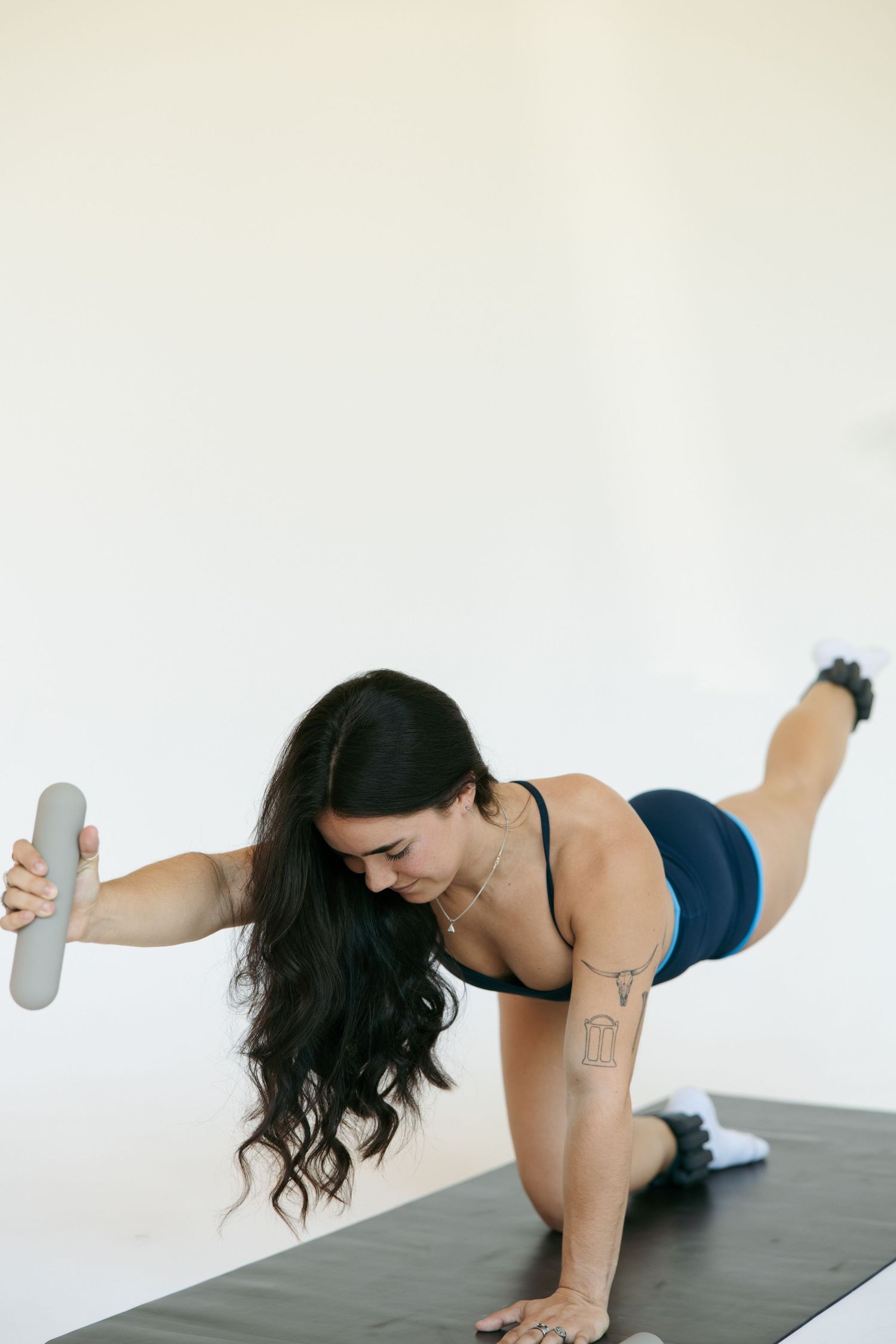 Woman performing a bird-dog exercise on a yoga mat, holding a dumbbell, wearing a blue sports outfit.