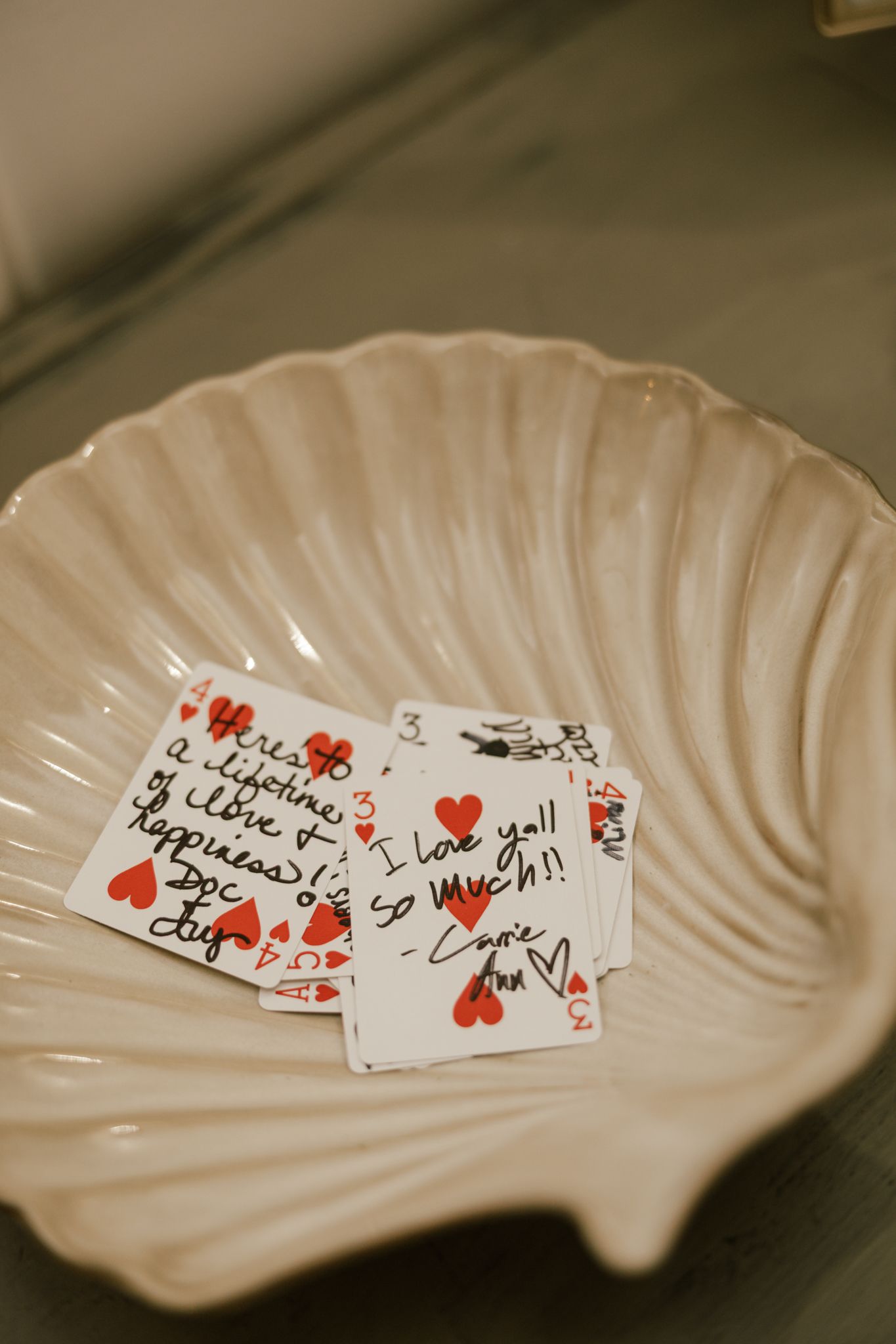 Signed playing cards with hearts and messages displayed on a white shell-shaped dish.