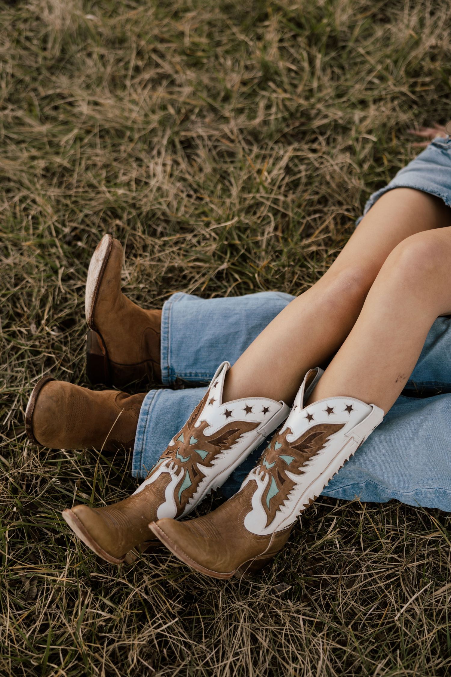 Close-up shots of feet wearing brown leather boots and white sneakers resting on dry grass.
