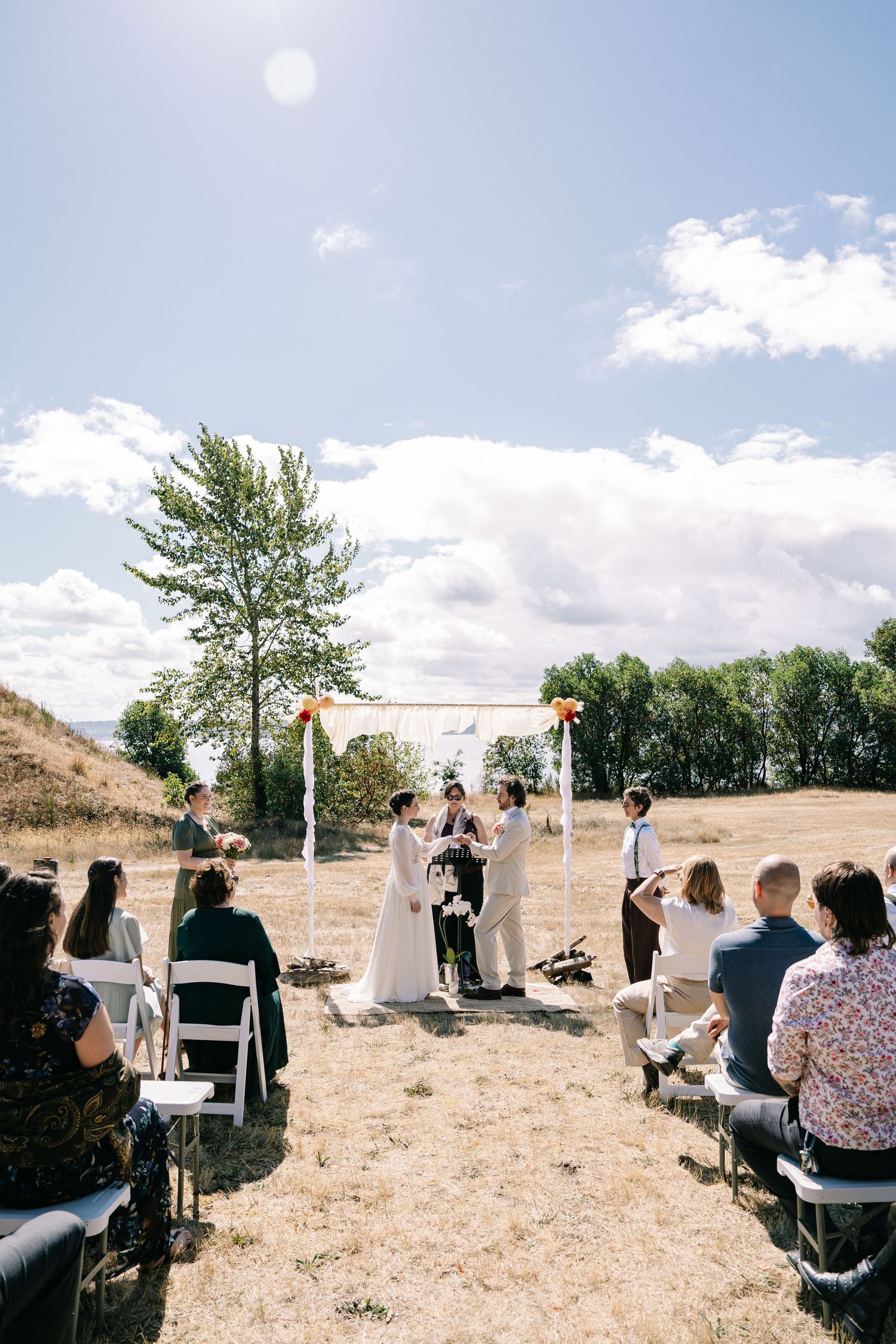 An outdoor wedding ceremony setup with white chairs on dry grass under a bright blue sky.