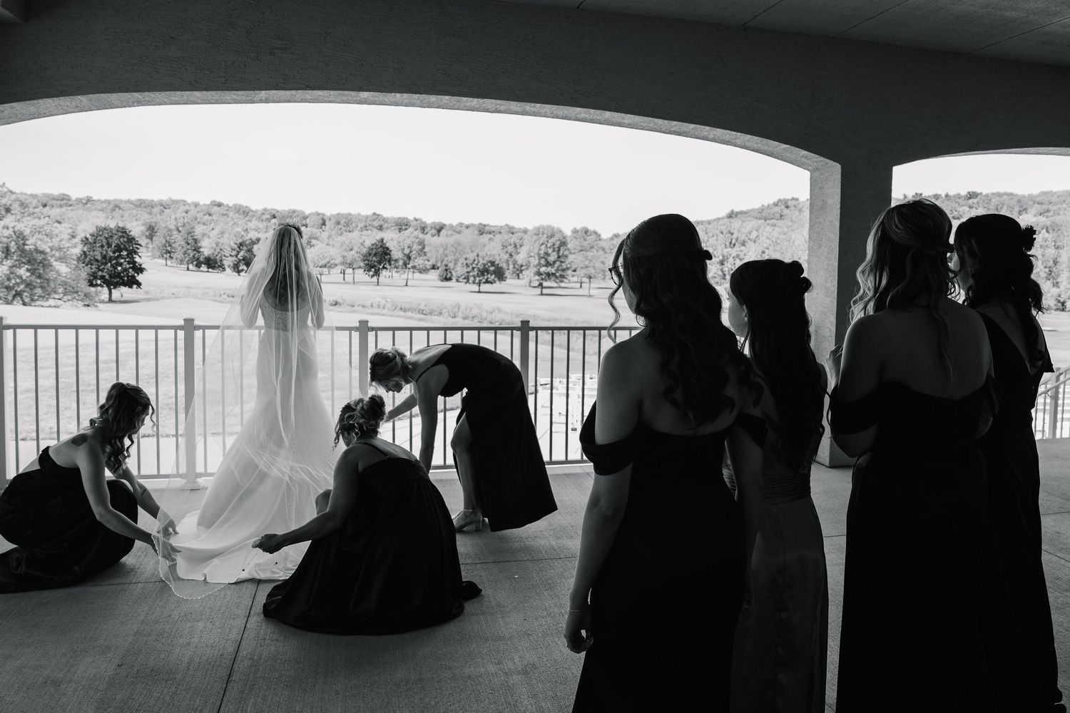 A series of silhouetted figures gathered in a covered outdoor gallery or walkway with natural lighting.
