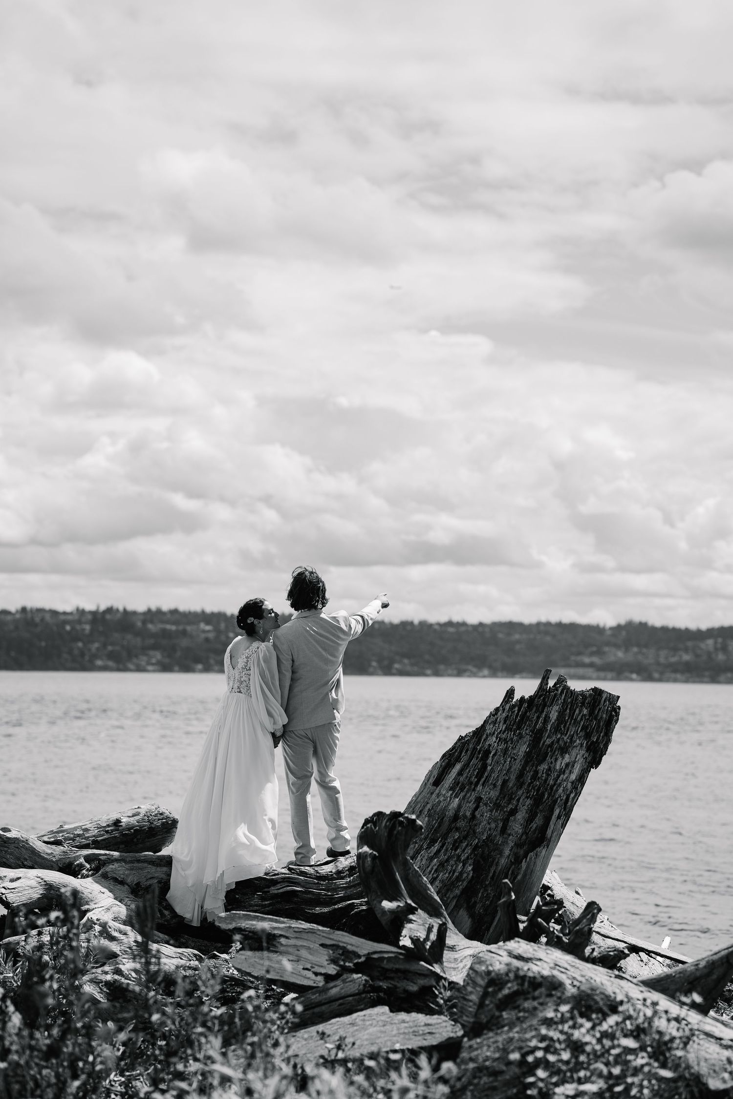 Black and white coastal landscape with couple sitting on rocky shore overlooking water.