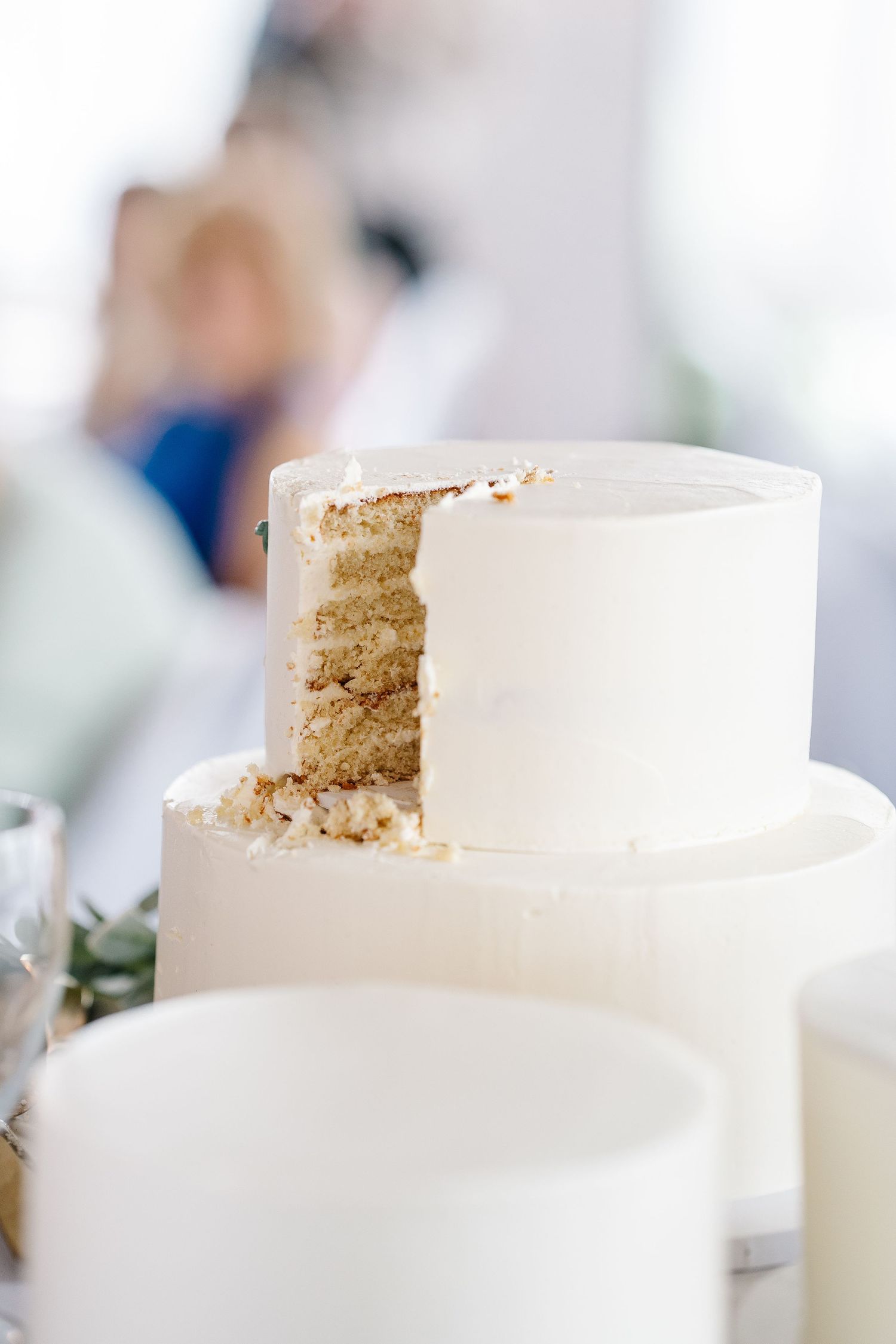 A white tiered wedding cake with vanilla buttercream frosting shows a slice removed revealing moist vanilla cake layers inside.