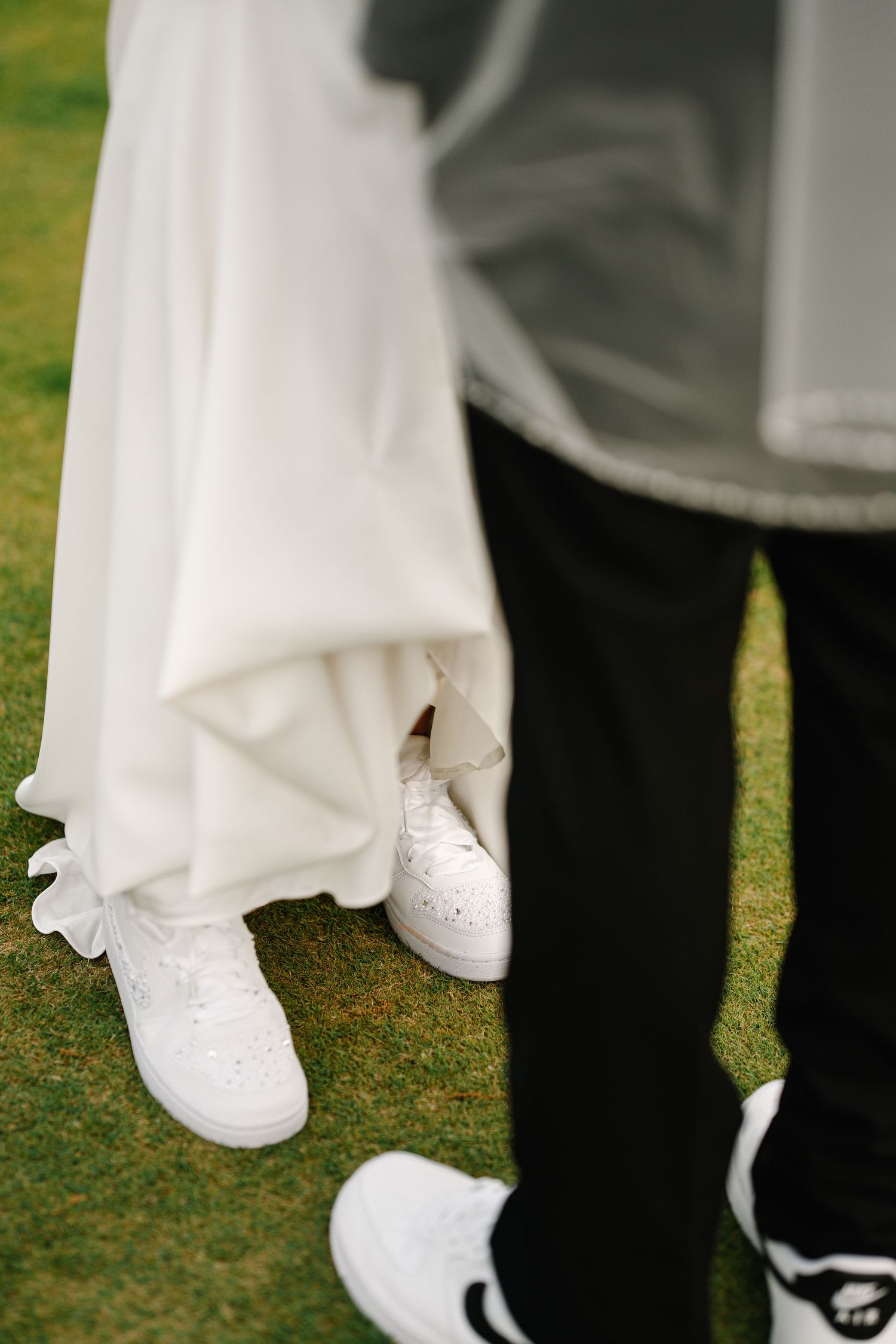 Wedding footwear detail shots showing white bridal shoes and black formal shoes on grass.