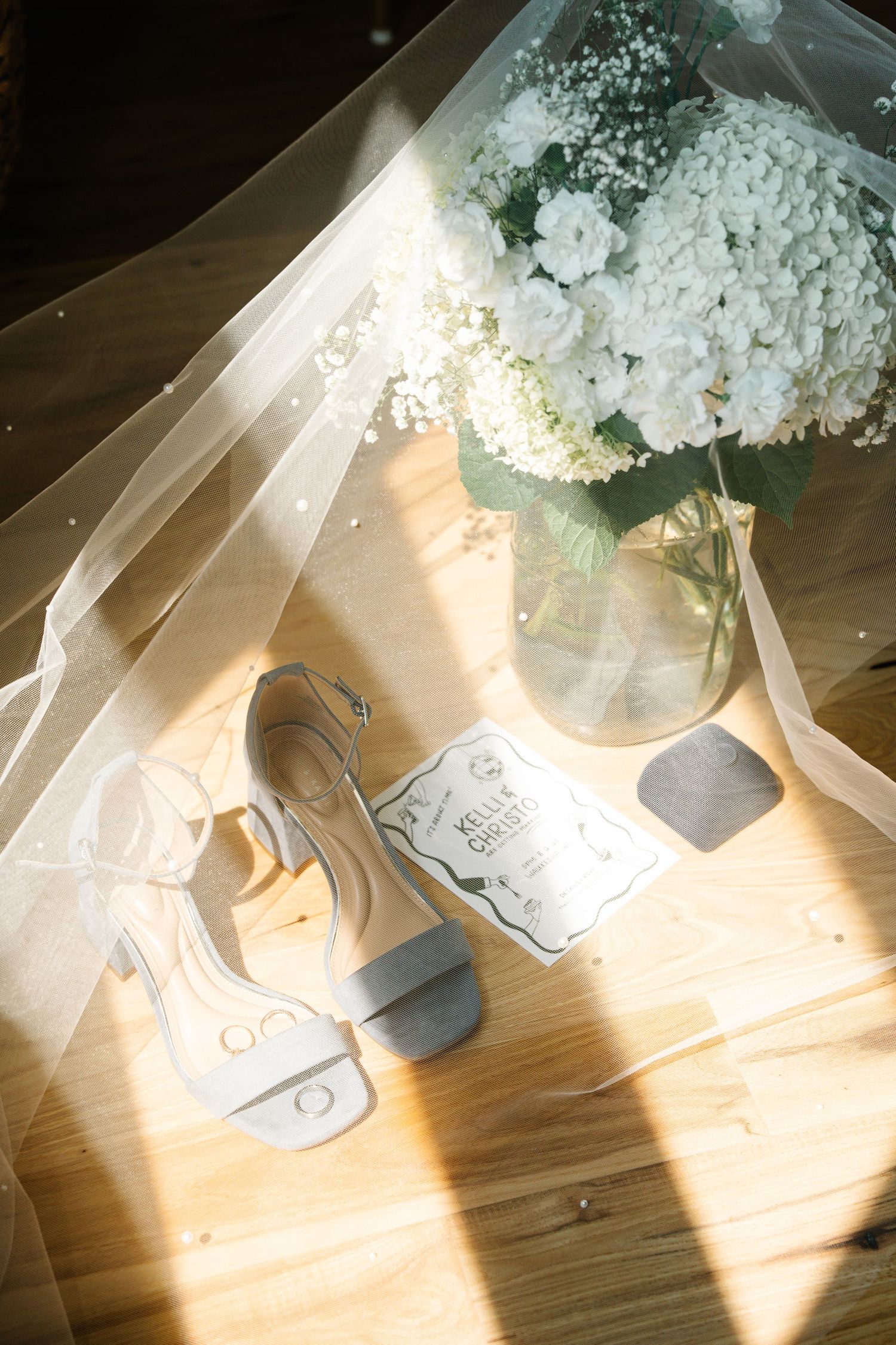 White flowers in a vase cast dramatic shadows across a wooden surface in natural sunlight.