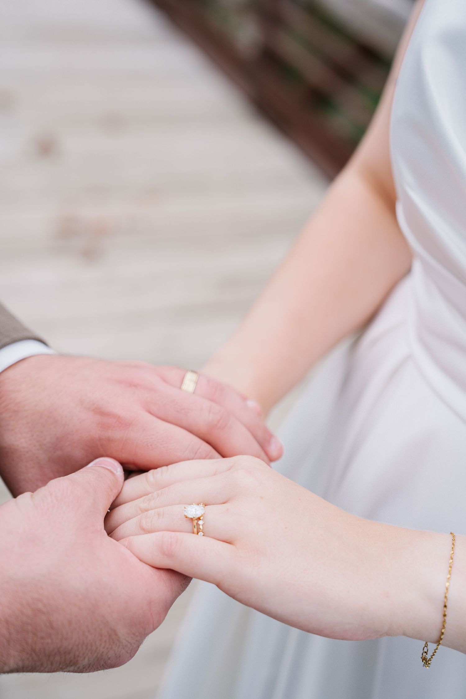 Close-up of hands exchanging wedding rings during ceremony, with bride wearing white dress and delicate bracelet.