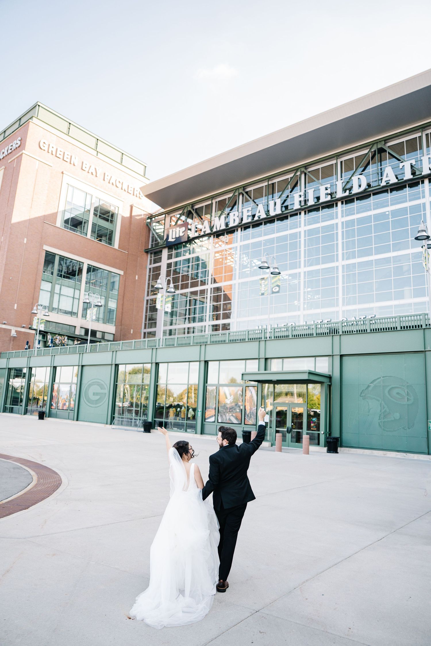 Couple celebrating outside modern glass building with raised arms.