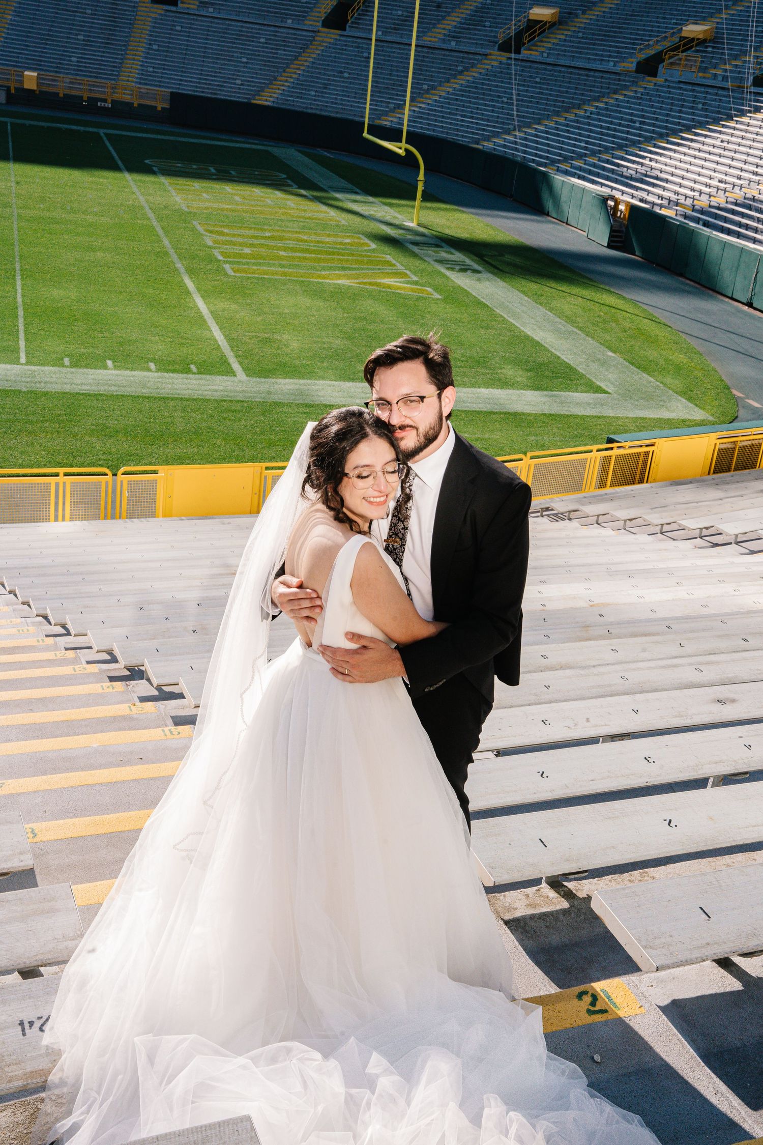 A wedding couple poses for romantic photos on the bleachers of a large football stadium on their special day.