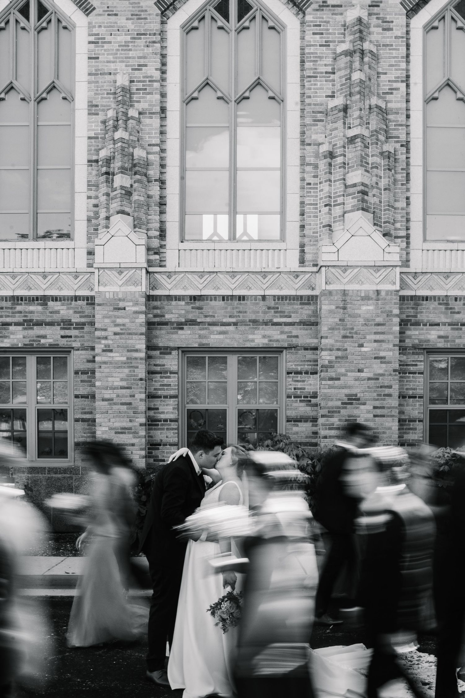 Blurred motion of people walking past a gothic stone building facade in black and white photography.