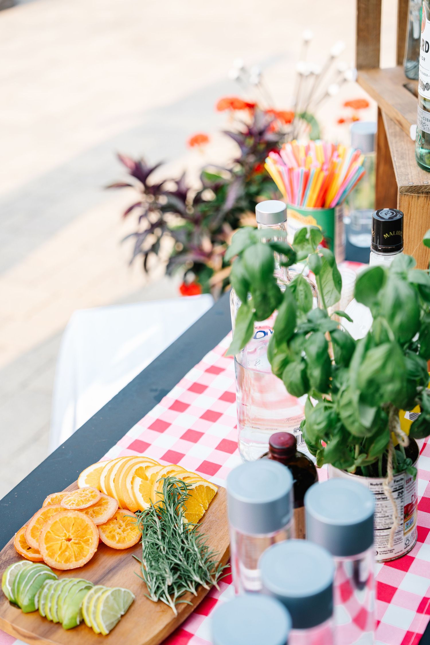 Fresh citrus slices and avocado on wooden cutting board with red checkered tablecloth and decorative bottles.