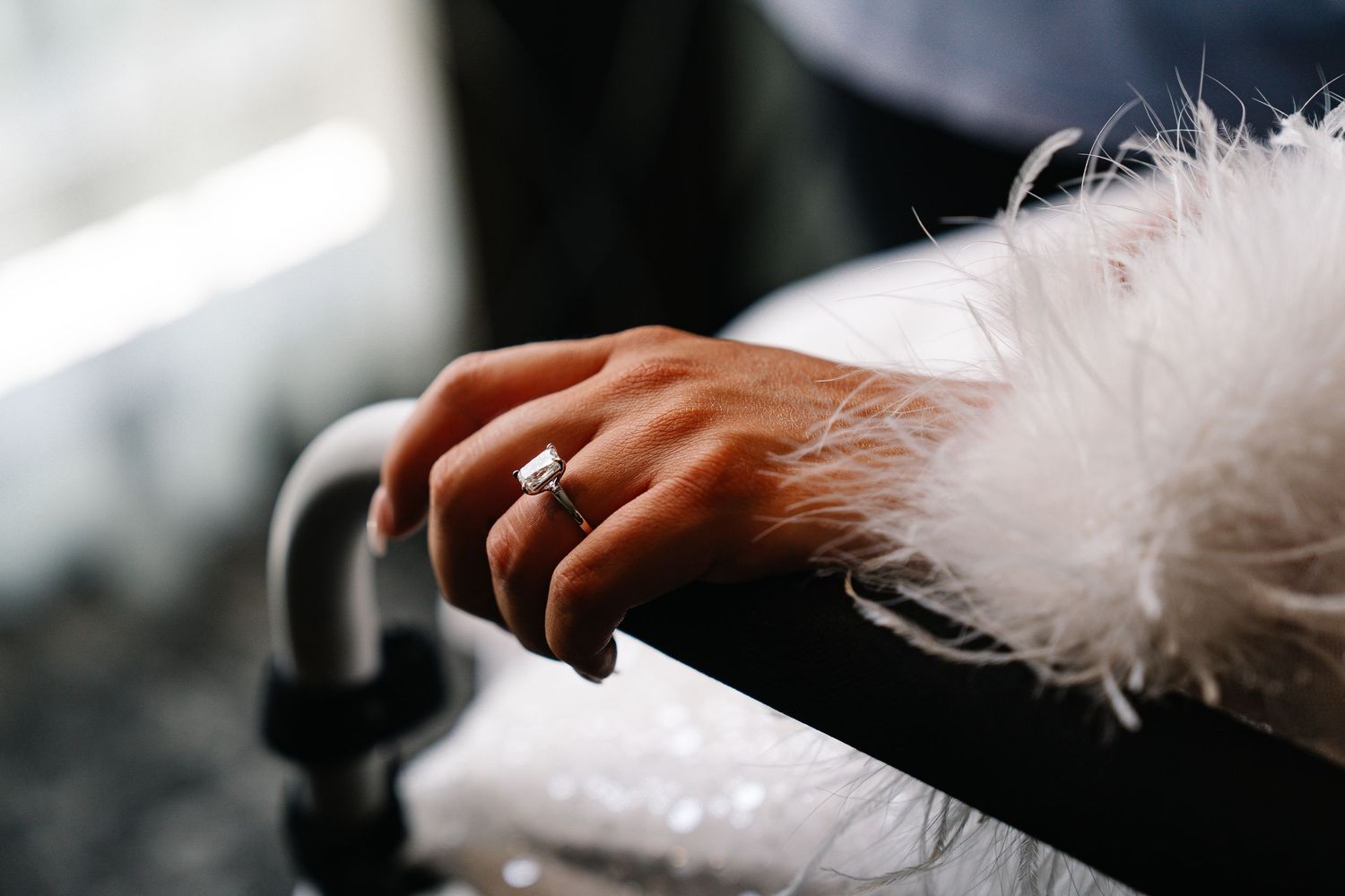 A fluffy white feather being held against a blurred dark background.