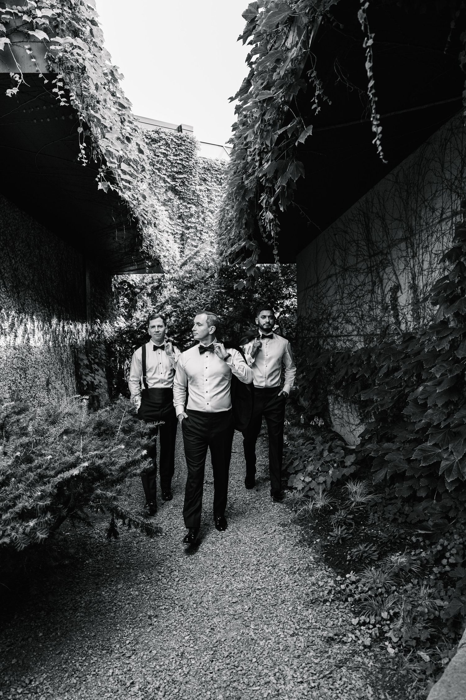 Black and white photo of three people walking through a narrow path between tall rock walls covered in vegetation.