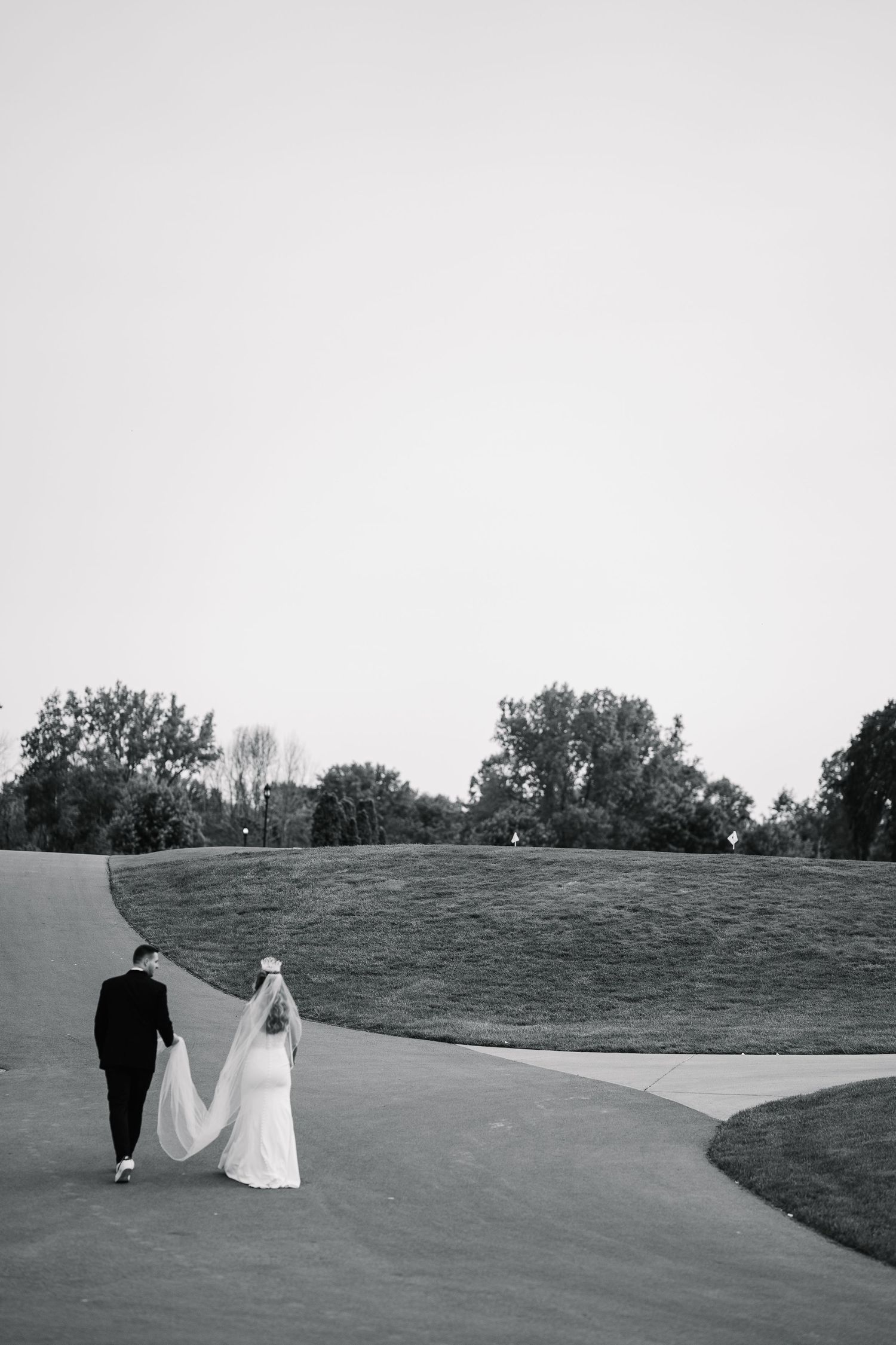 A couple walking along a curved path on a grassy hillside captured in black and white photography.