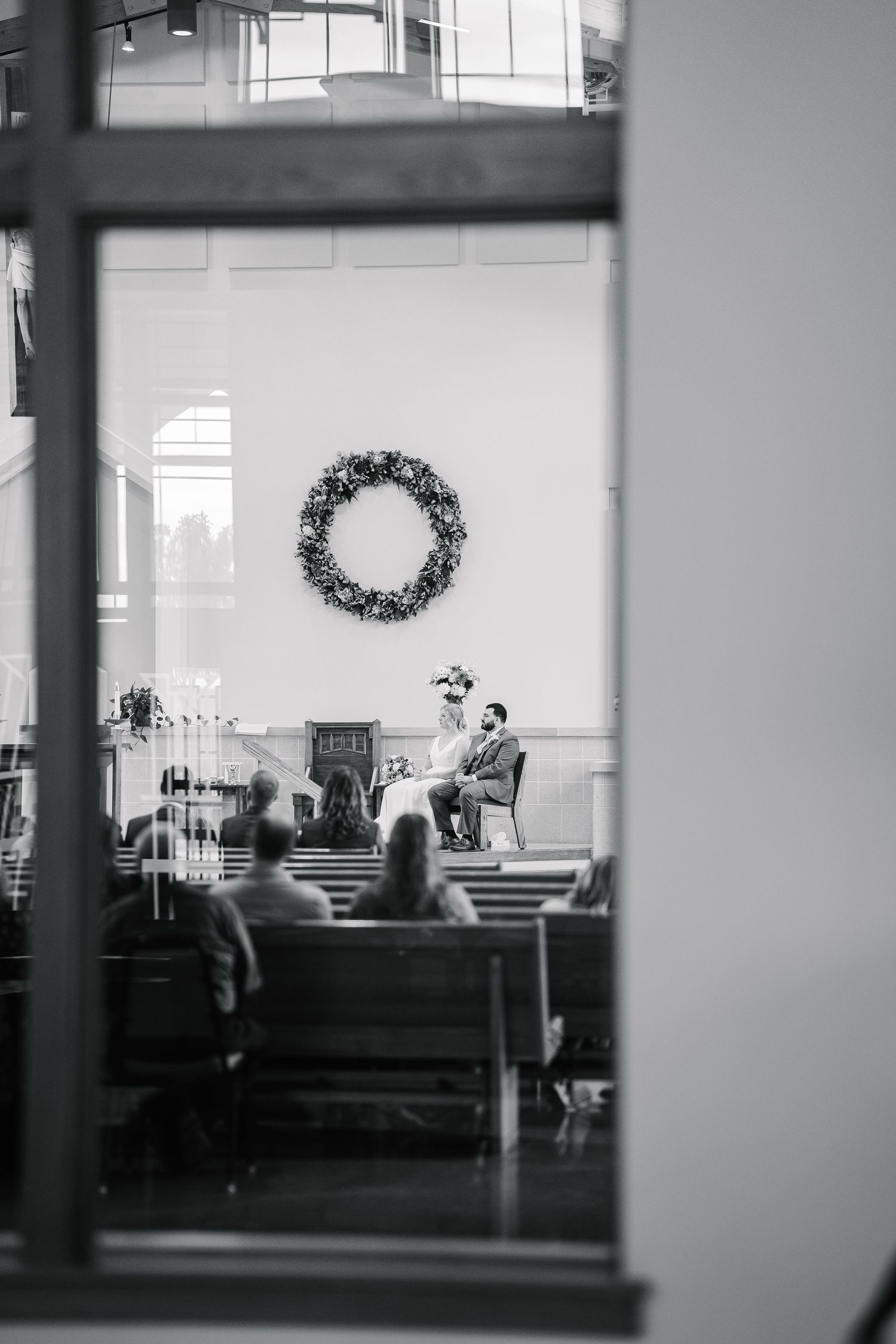 A black and white interior view of a church sanctuary with pews and a decorative wreath visible in soft focus.