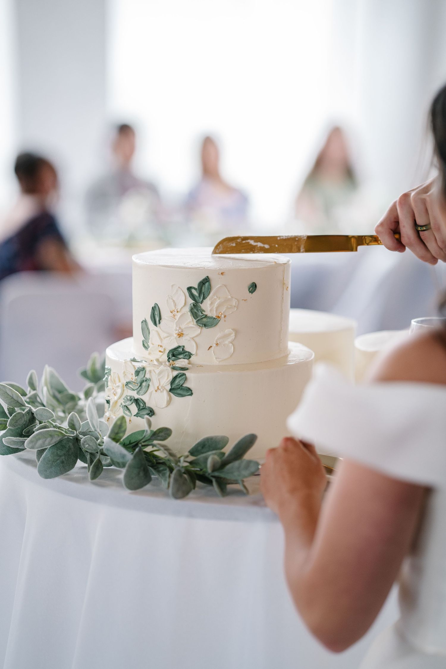 A white wedding cake decorated with delicate green eucalyptus leaves and foliage creates an elegant botanical design.