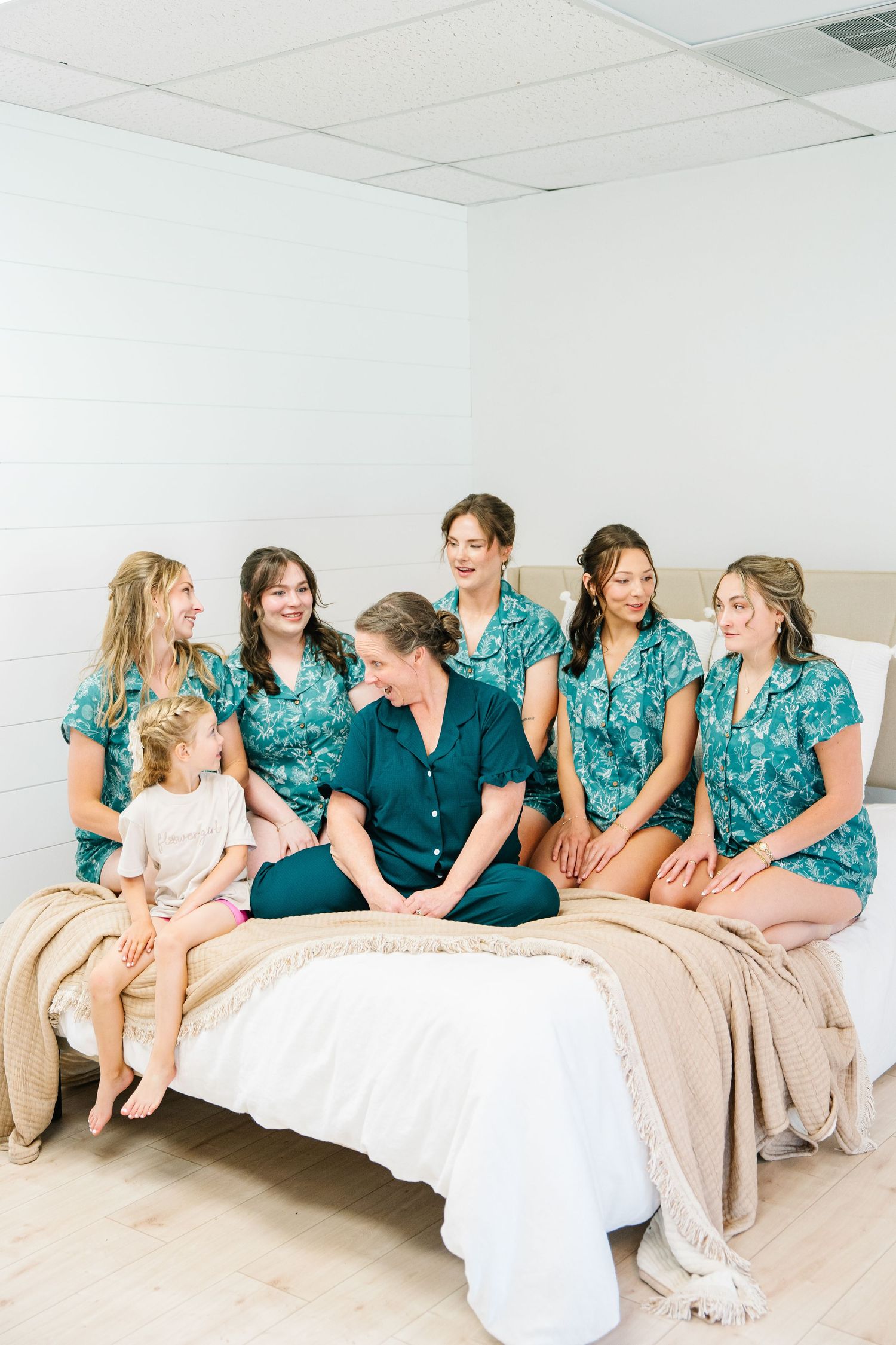 A group in matching turquoise floral dresses sits together on a white couch, creating a panoramic series of photos.