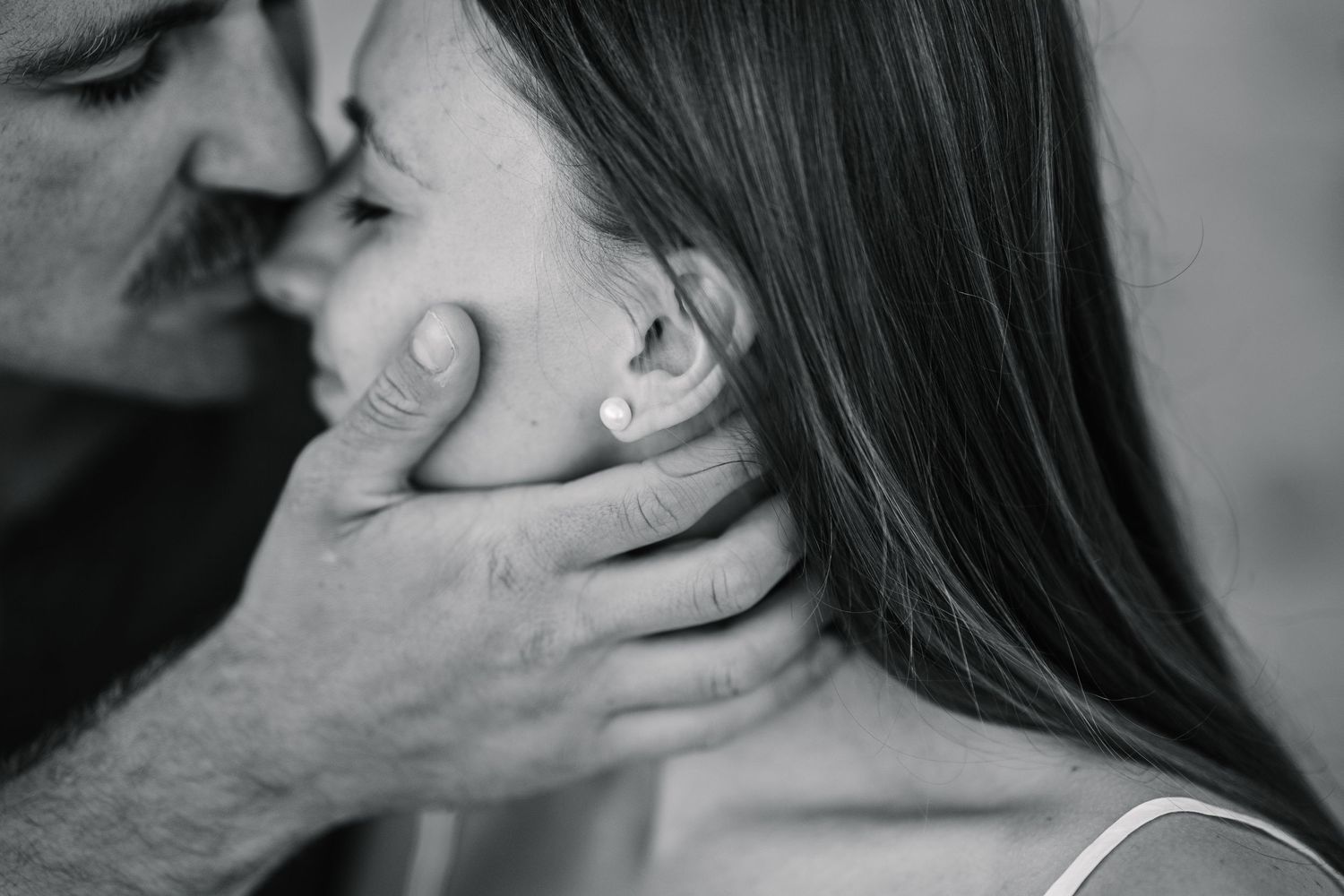 Black and white romantic photo of a man tenderly holding a woman's face while leaning in to kiss her.