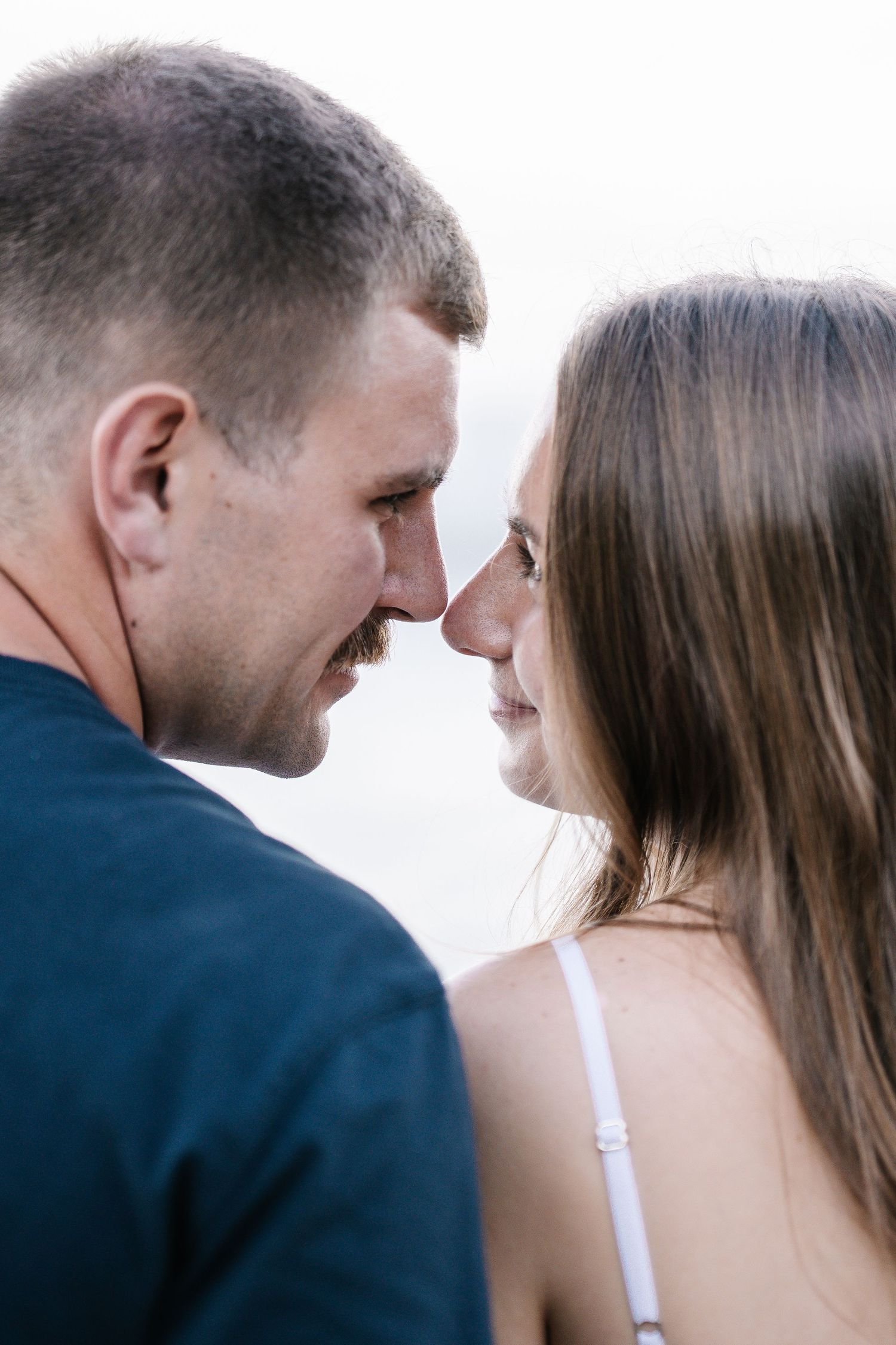 A romantic couple sharing an intimate nose-to-nose moment, gazing into each other's eyes outdoors.