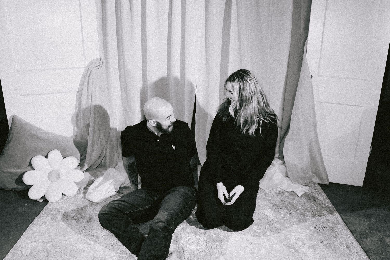 Black and white photo of two people sitting on floor with white balloons in dark moody setting.