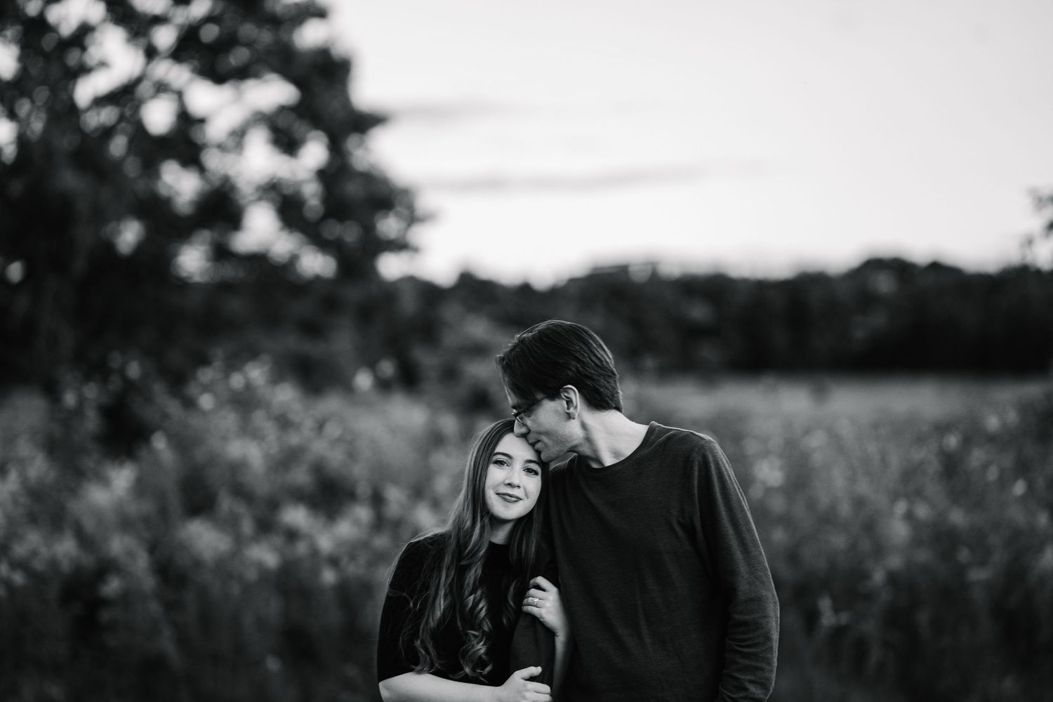 A couple shares an intimate moment in a black and white outdoor portrait session among tall grasses and natural scenery.