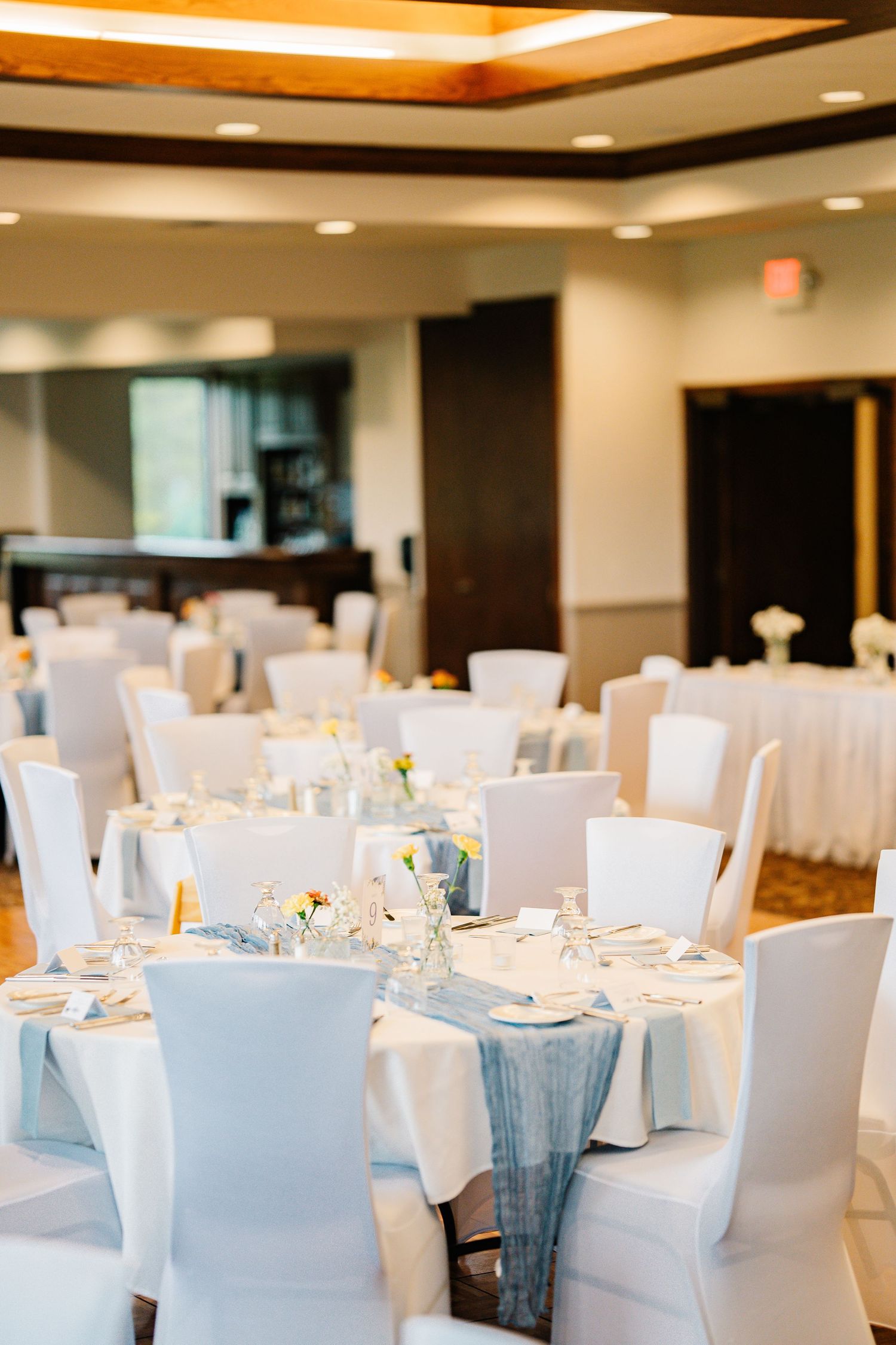Elegant wedding reception venue with white-clothed tables and chairs decorated in soft blue accents and ambient lighting.