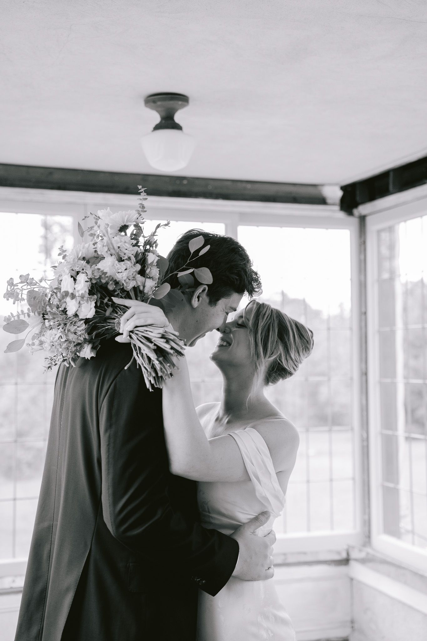 A romantic black and white photograph of a loving couple sharing a tender moment while holding a floral bouquet.