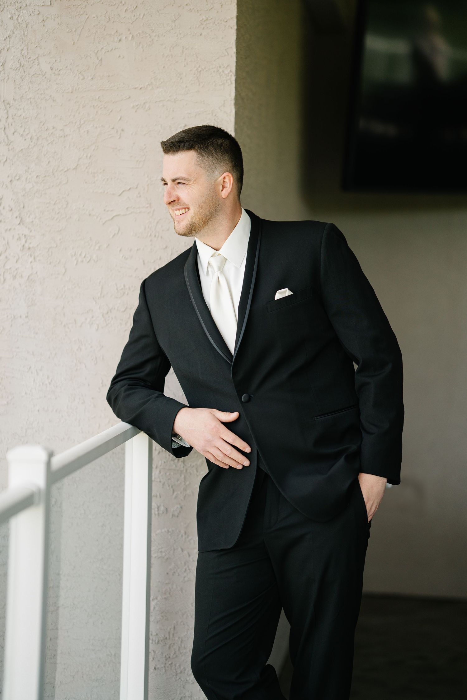 Groom in classic black tuxedo poses against white wall in series of cropped detail shots.