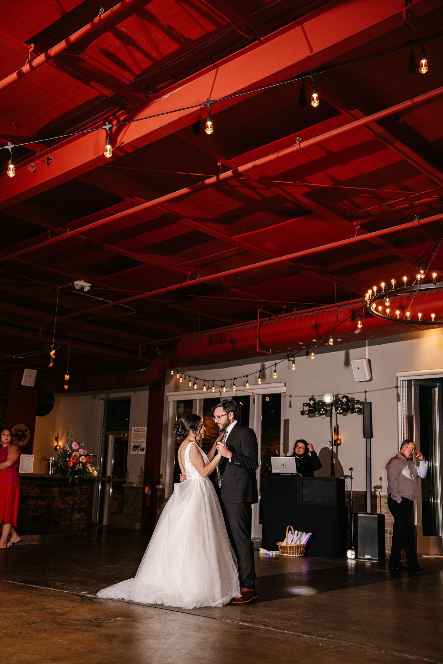 Wedding reception venue with red ceiling lighting and string lights showing dance floor and guests.