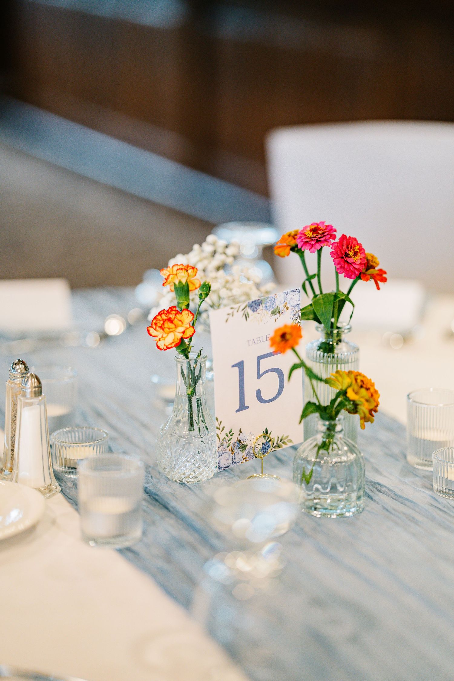 Small glass vases with colorful ranunculus flowers and tea lights create an elegant table setting at a wedding reception.