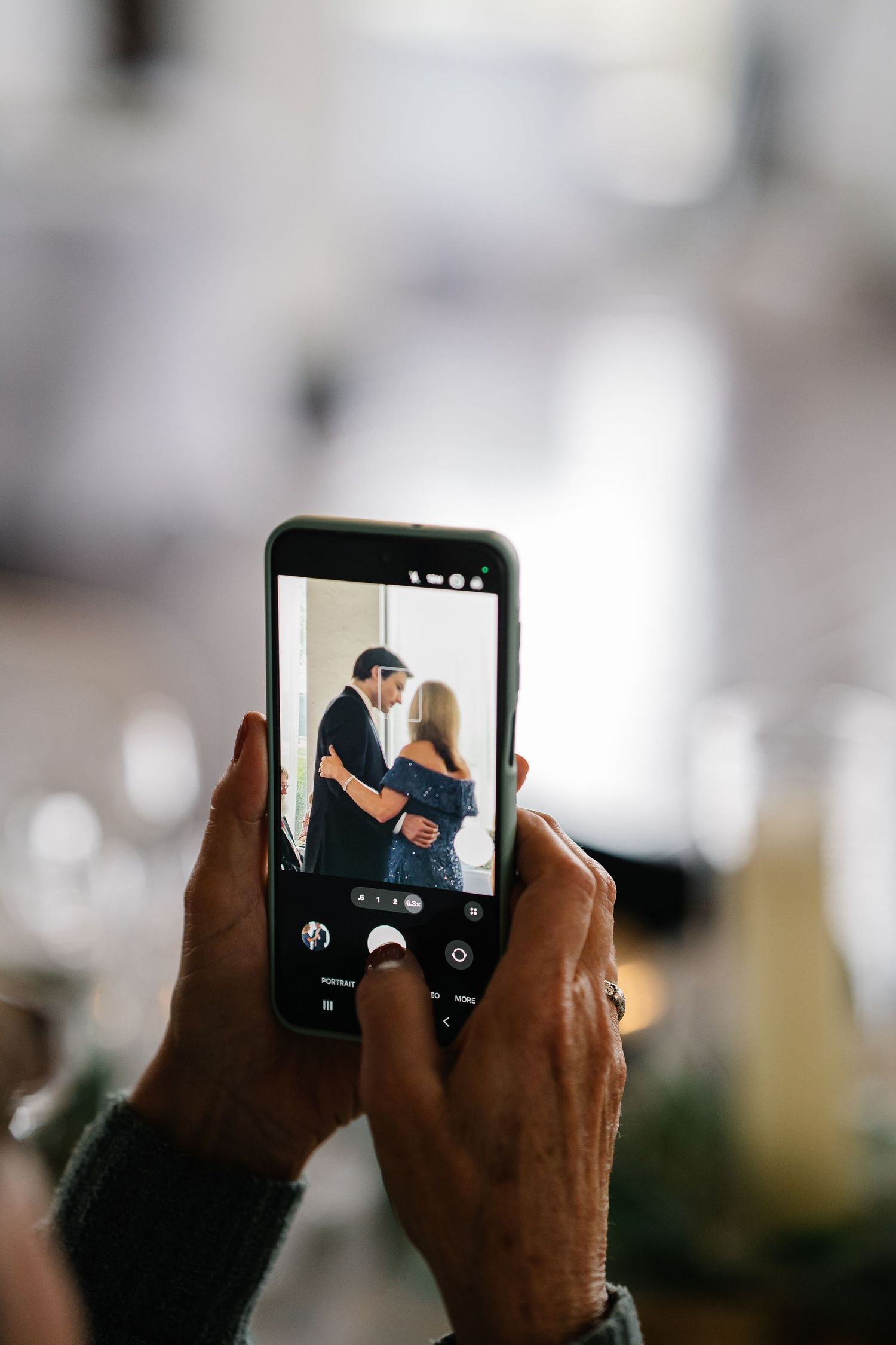 Hands holding a smartphone taking photos of a couple in three sequential shots showing different angles and poses.