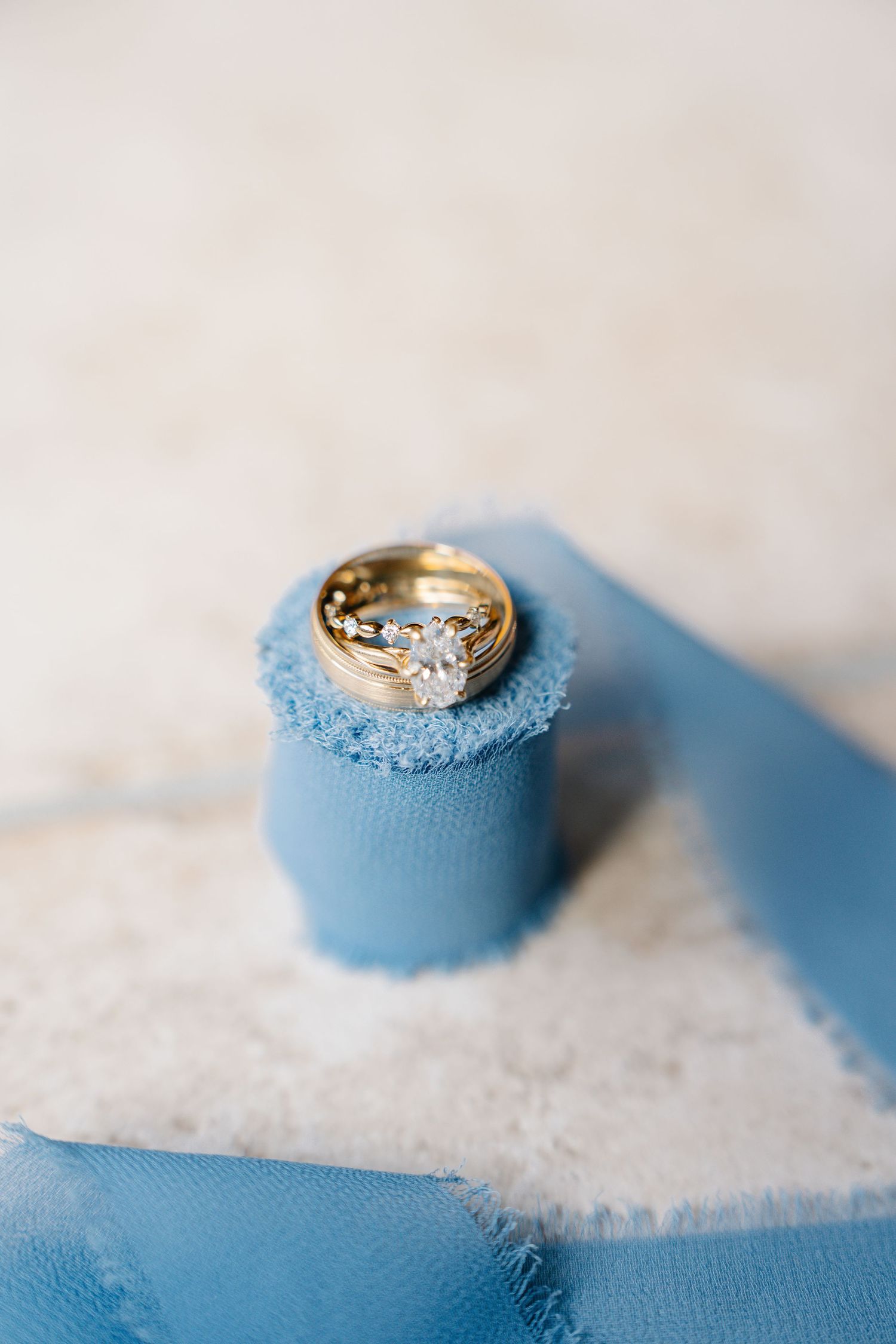 A gold diamond engagement ring rests on a light blue fabric with delicate white lace trim.