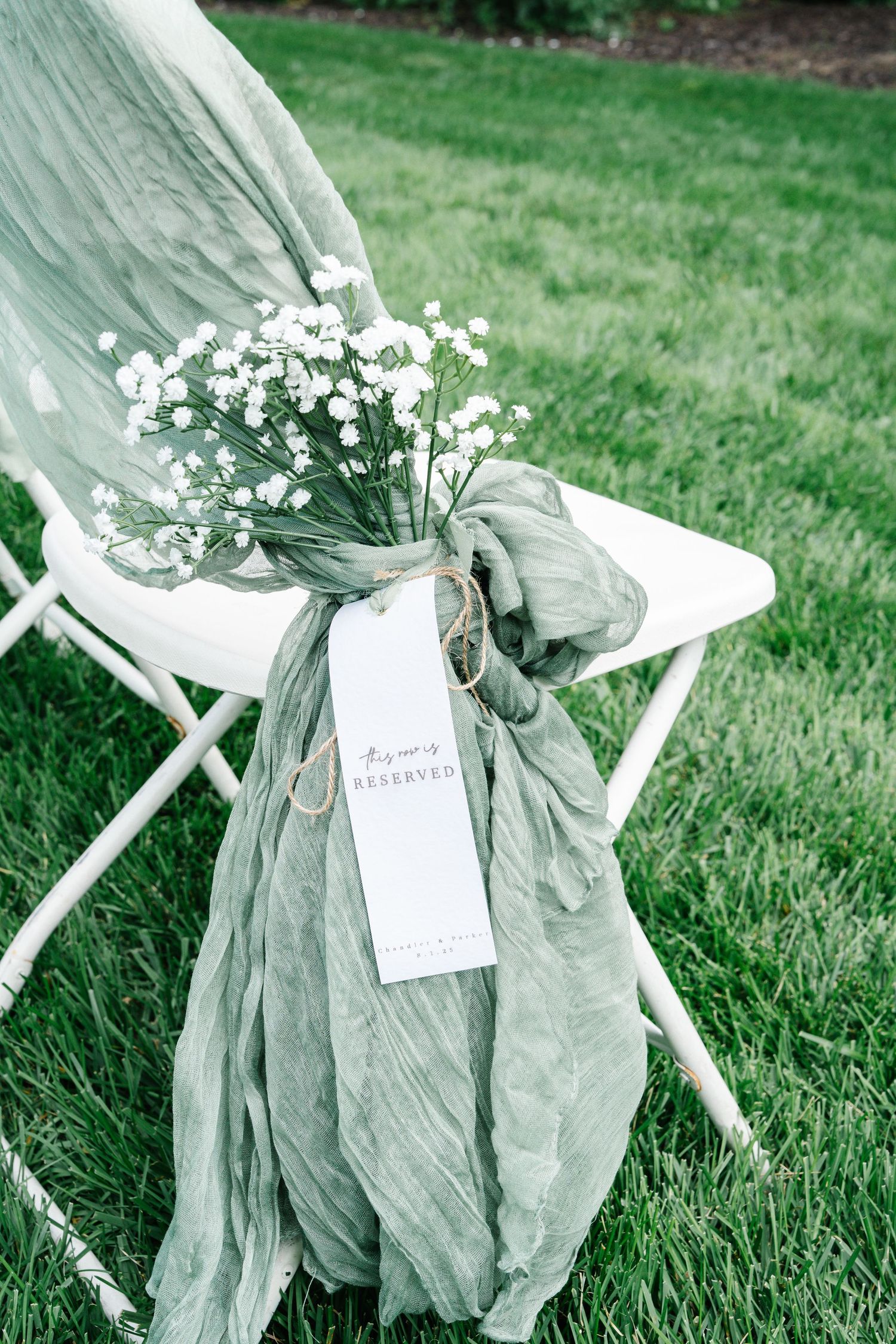 White linen chair decorations with floral arrangements and ribbons create an elegant outdoor wedding setting on green grass.