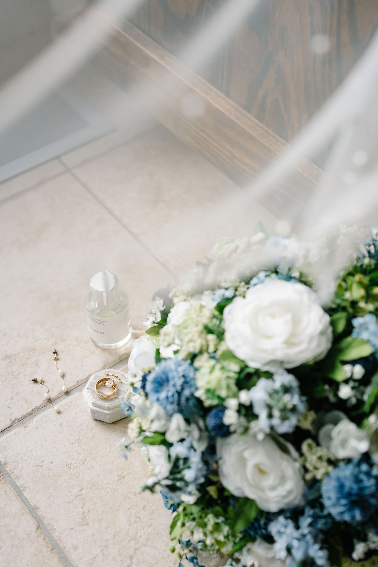 A delicate wedding bouquet featuring white roses and light blue hydrangeas arranged on a light textured surface.