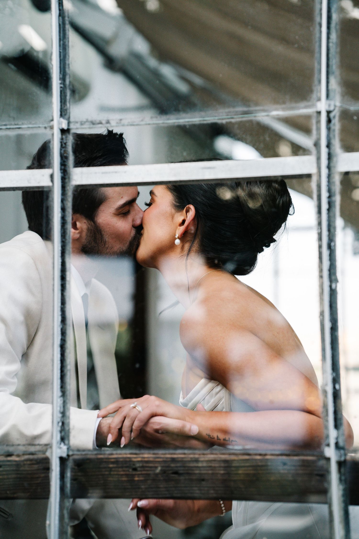 A romantic couple sharing a tender kiss through window panes in an artistic black and white composition.