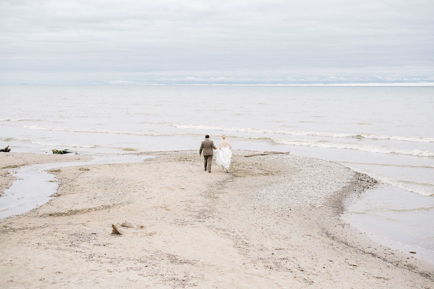 People walking along a misty beach shoreline with waves rolling in on an overcast day.