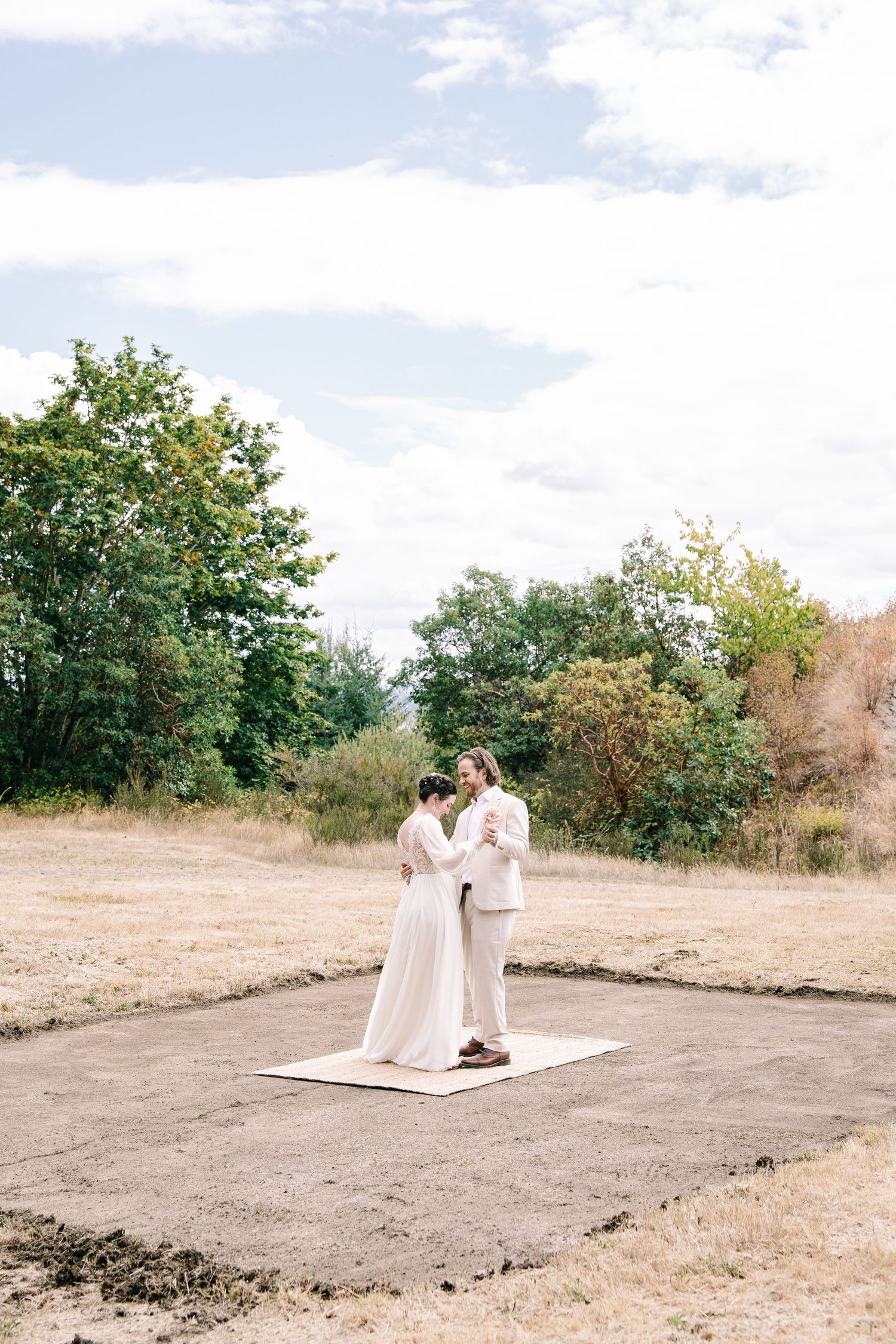 A couple shares an intimate moment on a white blanket in a scenic outdoor field setting.
