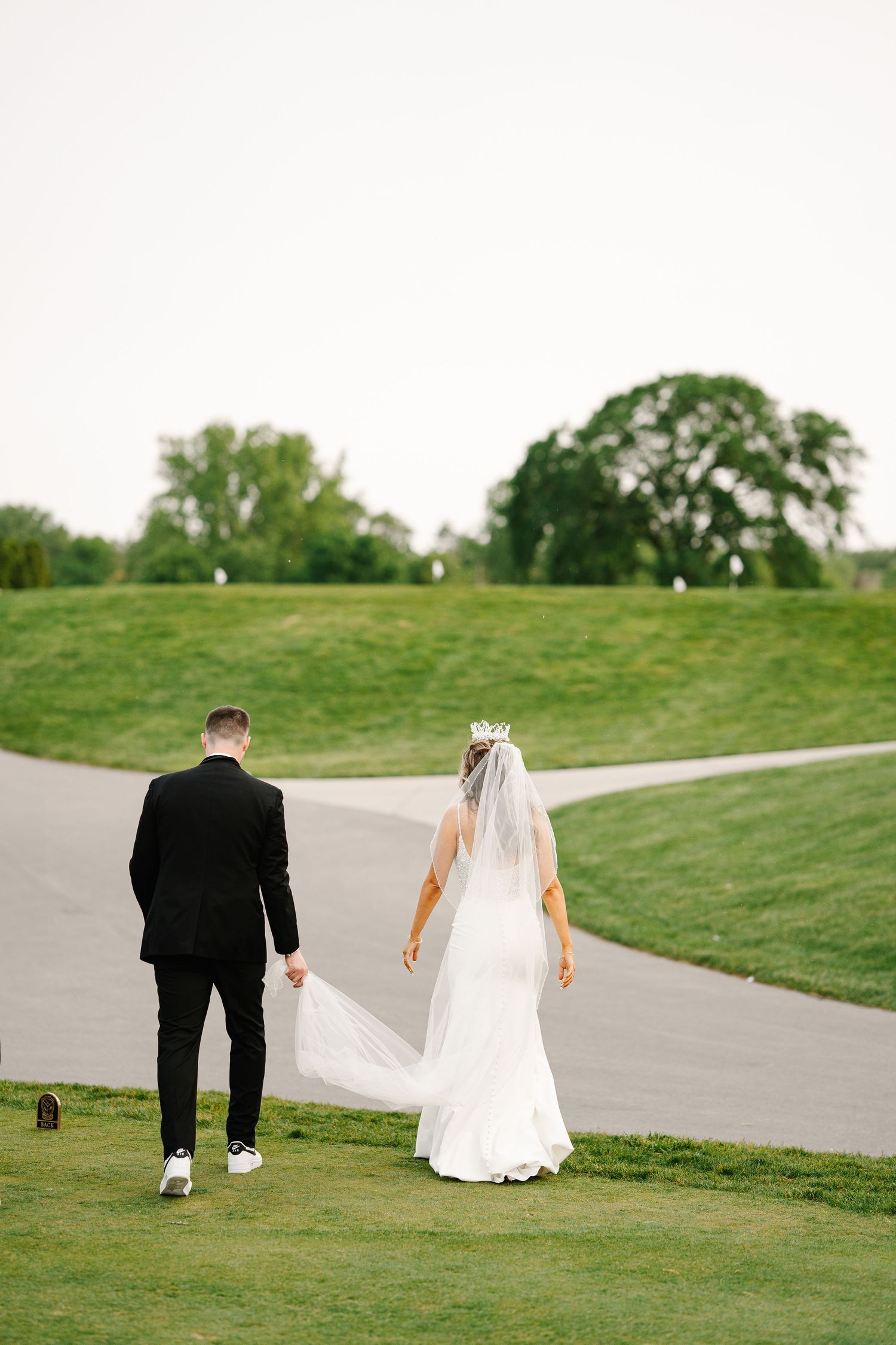 Newlyweds walking together on a winding path through green rolling hills.