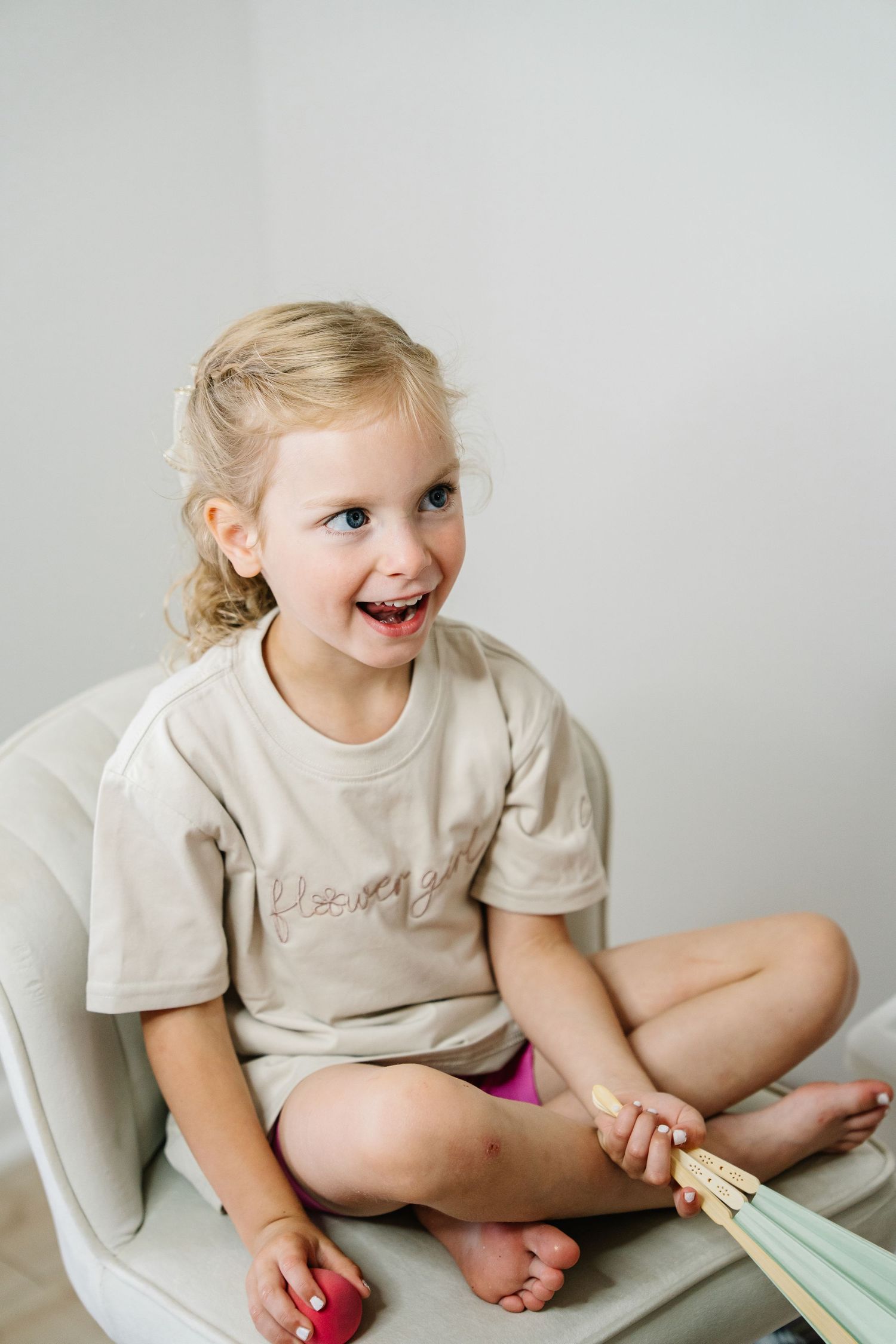 A child in a beige shirt sits cross-legged on a white surface while playing and laughing joyfully.