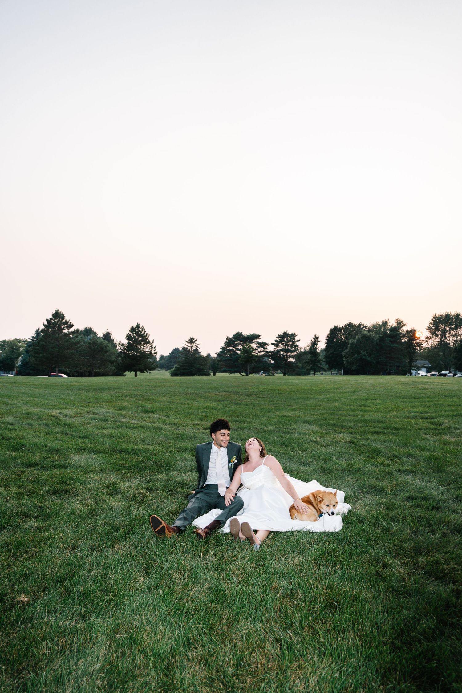A couple relaxes together on a blanket in a serene green meadow during sunset.
