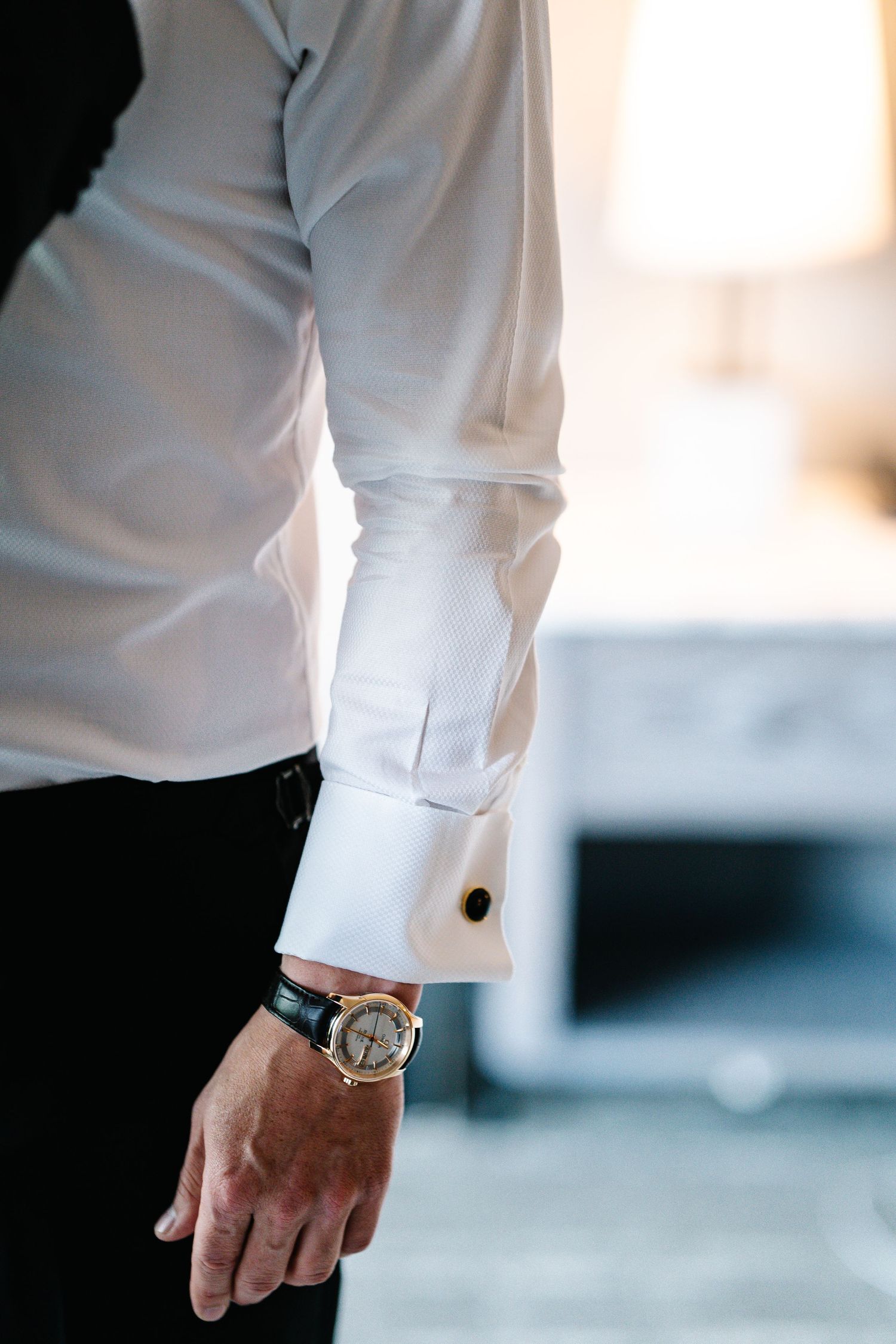 A person wearing a crisp white dress shirt with rolled-up sleeves and a luxury watch on their wrist.