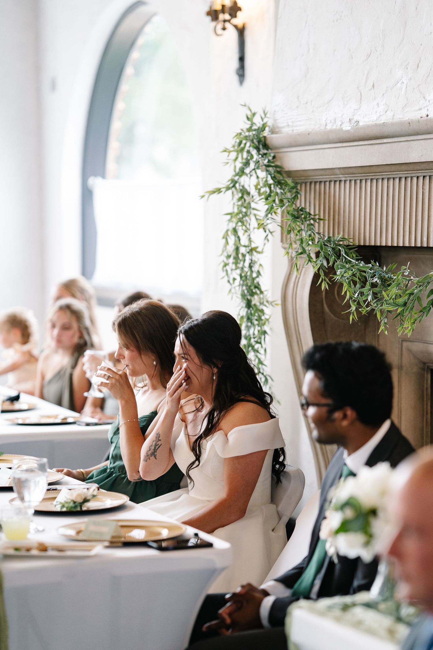 Wedding guests seated at elegant tables with white linens enjoy a reception dinner in a bright, airy venue.