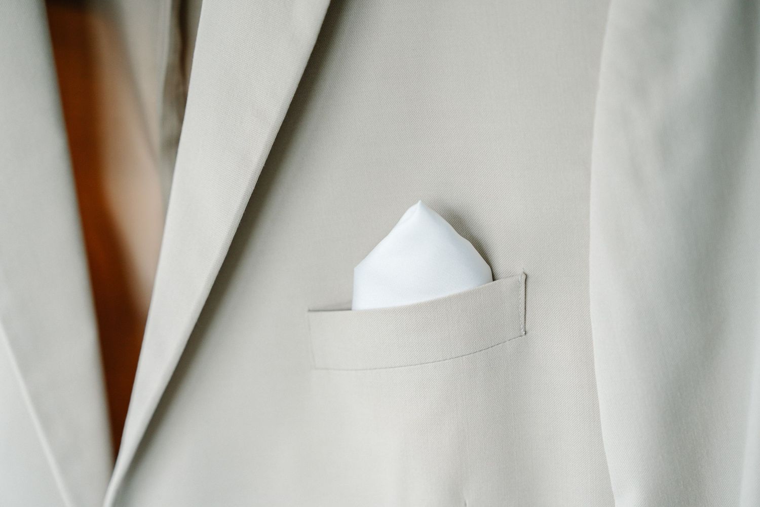 A white pocket square neatly folded into the breast pocket of a light beige suit jacket.