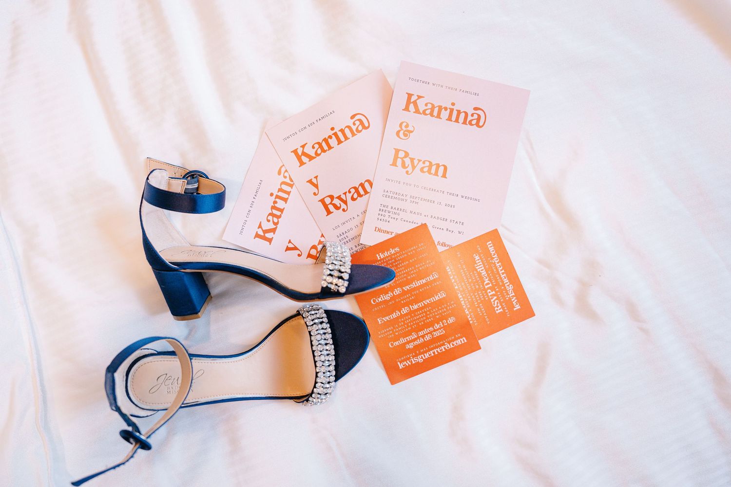 Wedding rings and orange name cards arranged on white linen with soft natural lighting.