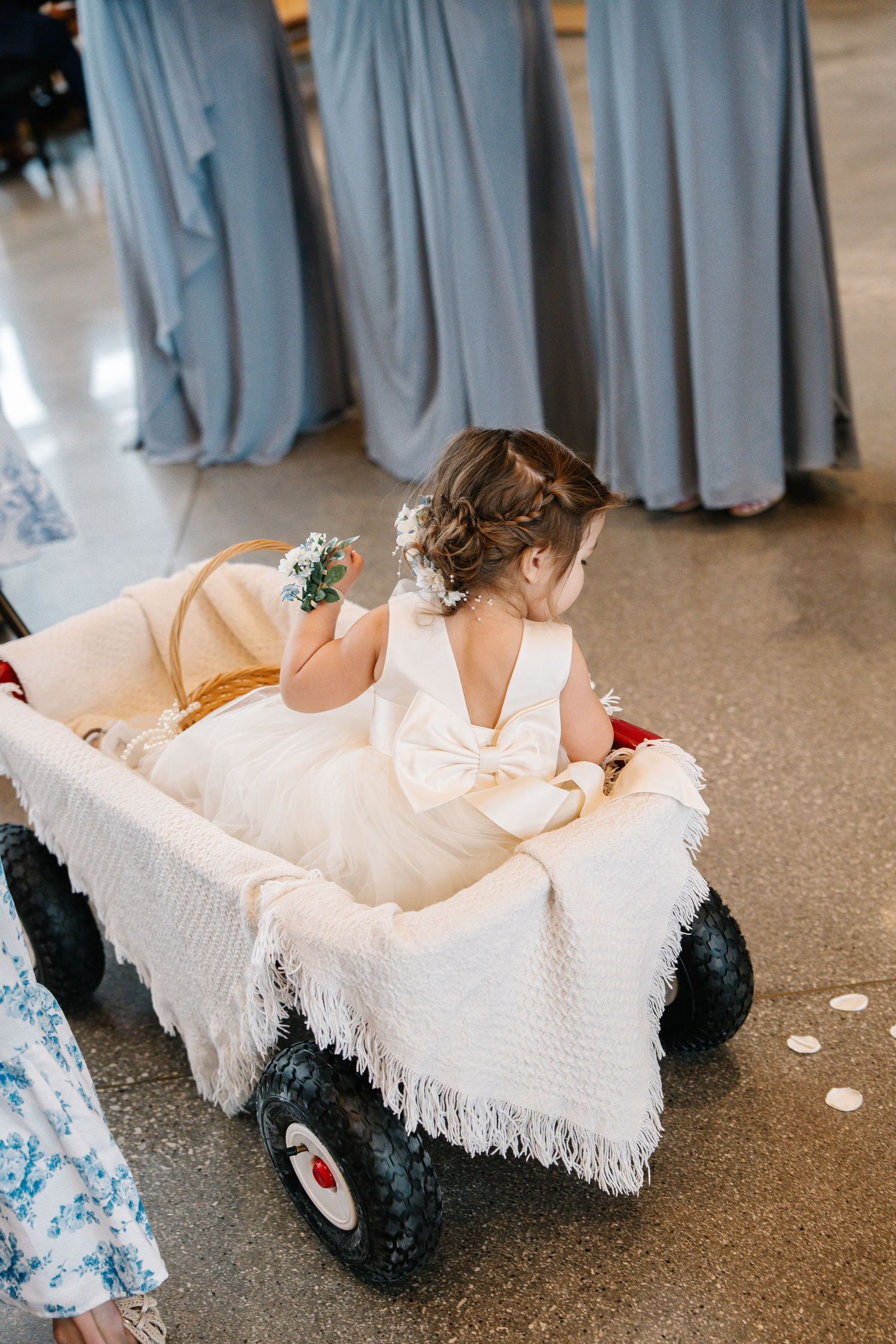 Bridesmaids wearing dusty blue dresses sit on white blankets showing their red shoes in a coordinated wedding photo.