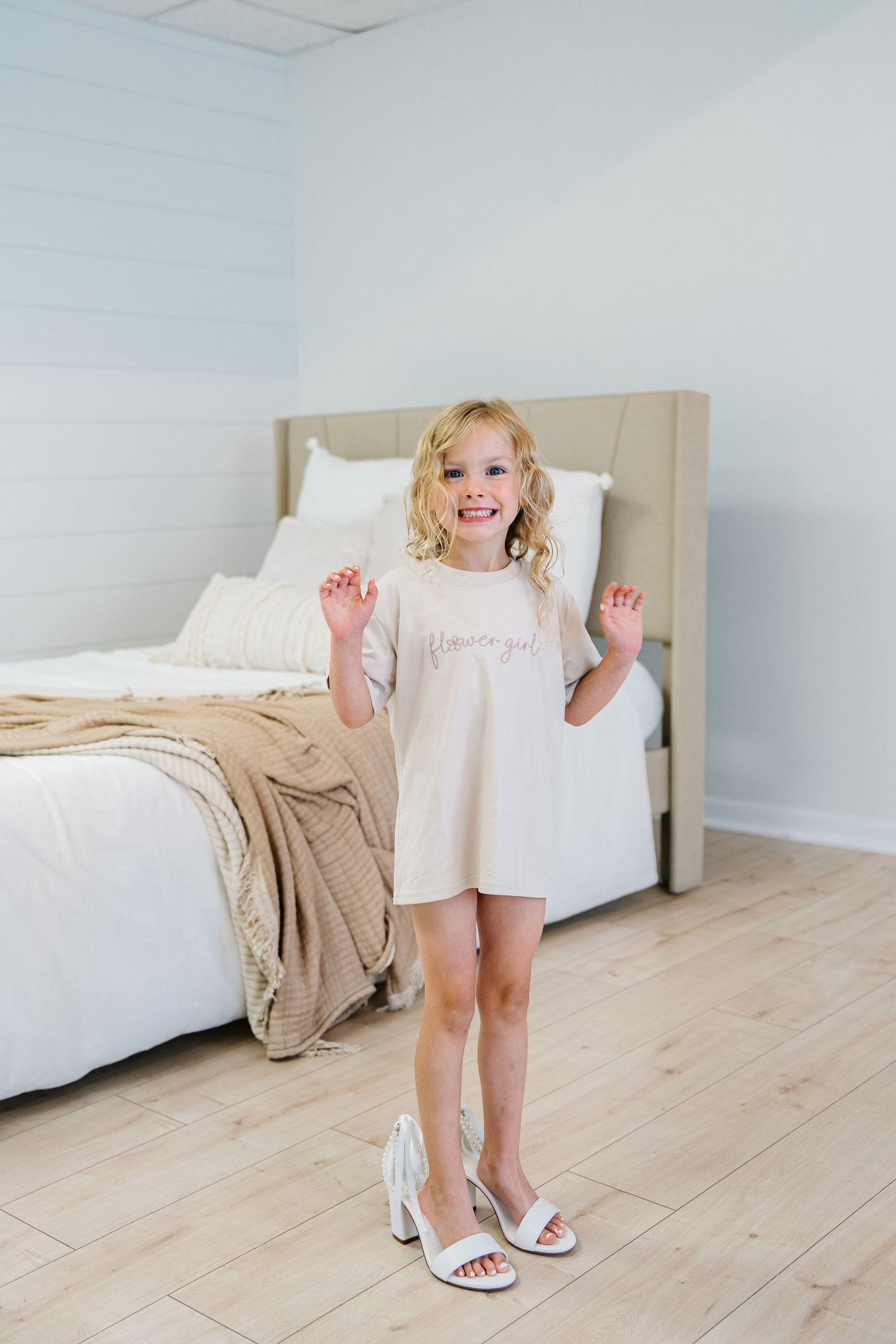 A series of four connected photos showing a child in a white dress and slippers standing against a minimalist bedroom wall.