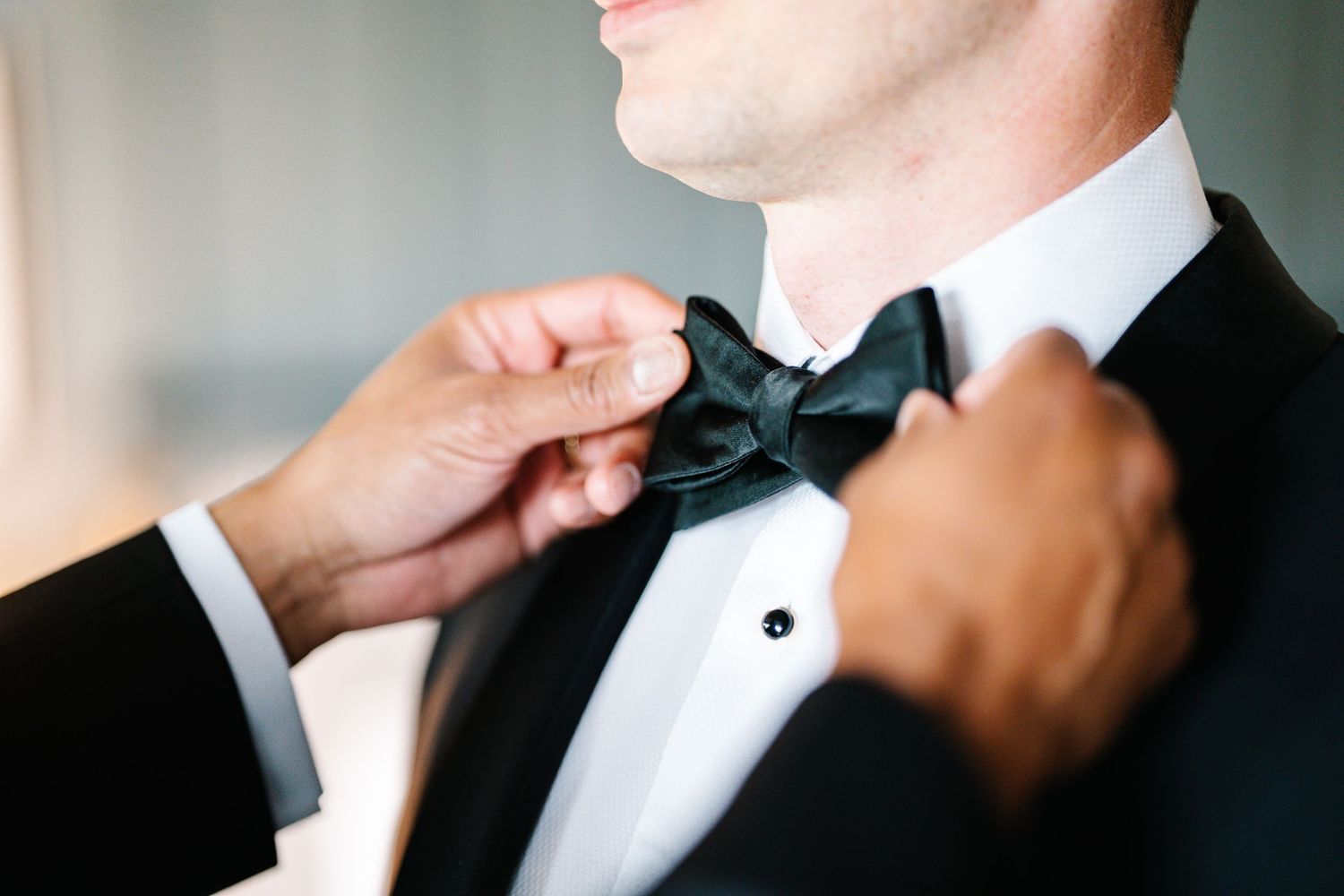 A groom adjusts his black bow tie while getting ready for a formal event.